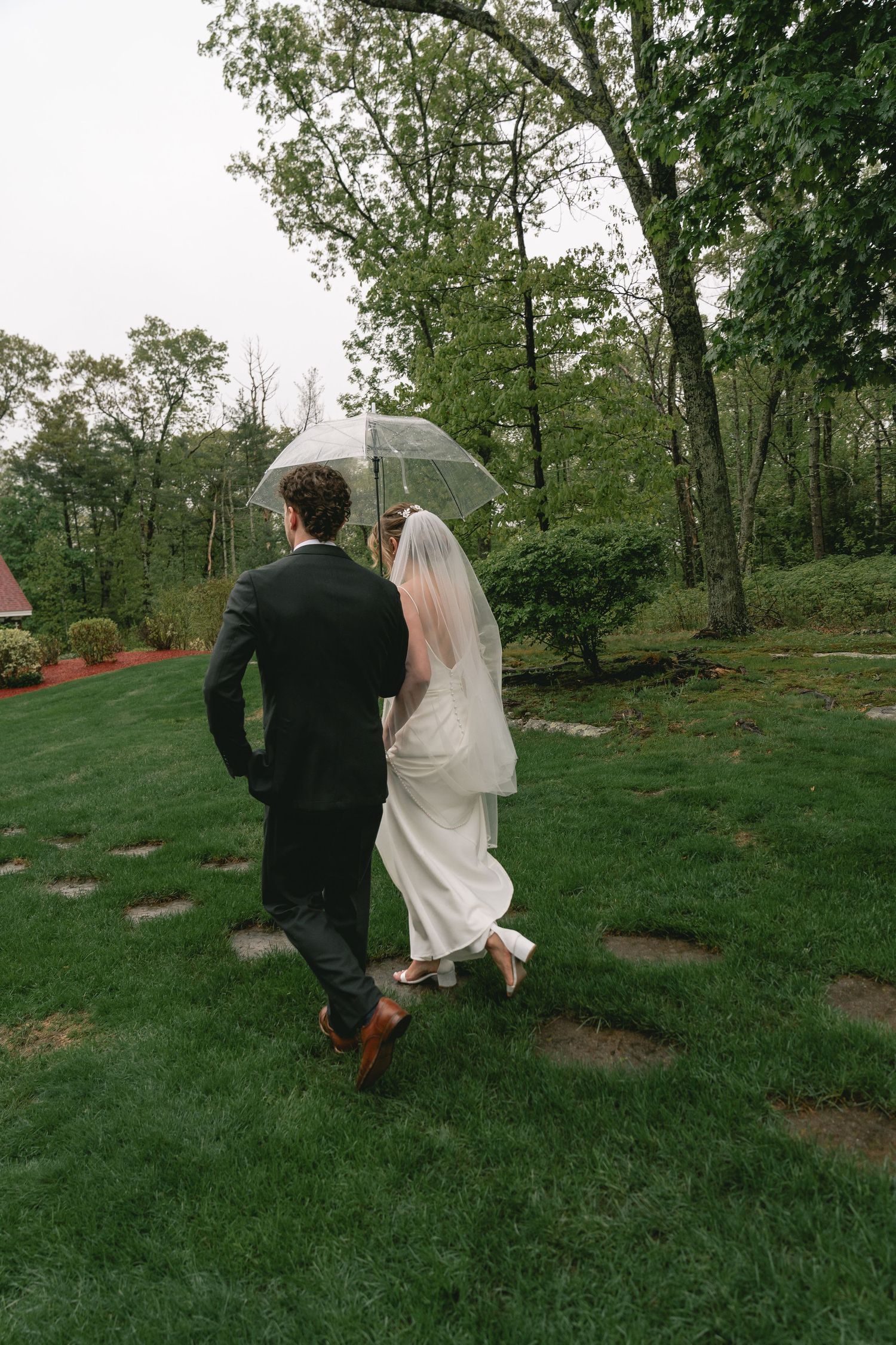 Newlyweds walk hand in hand across a grassy hillside on their wedding day.