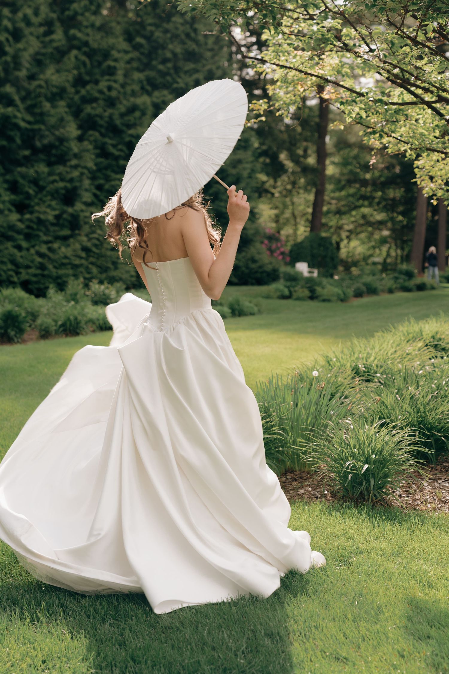 A flowing white wedding dress twirls gracefully in a lush garden setting with a decorative parasol.