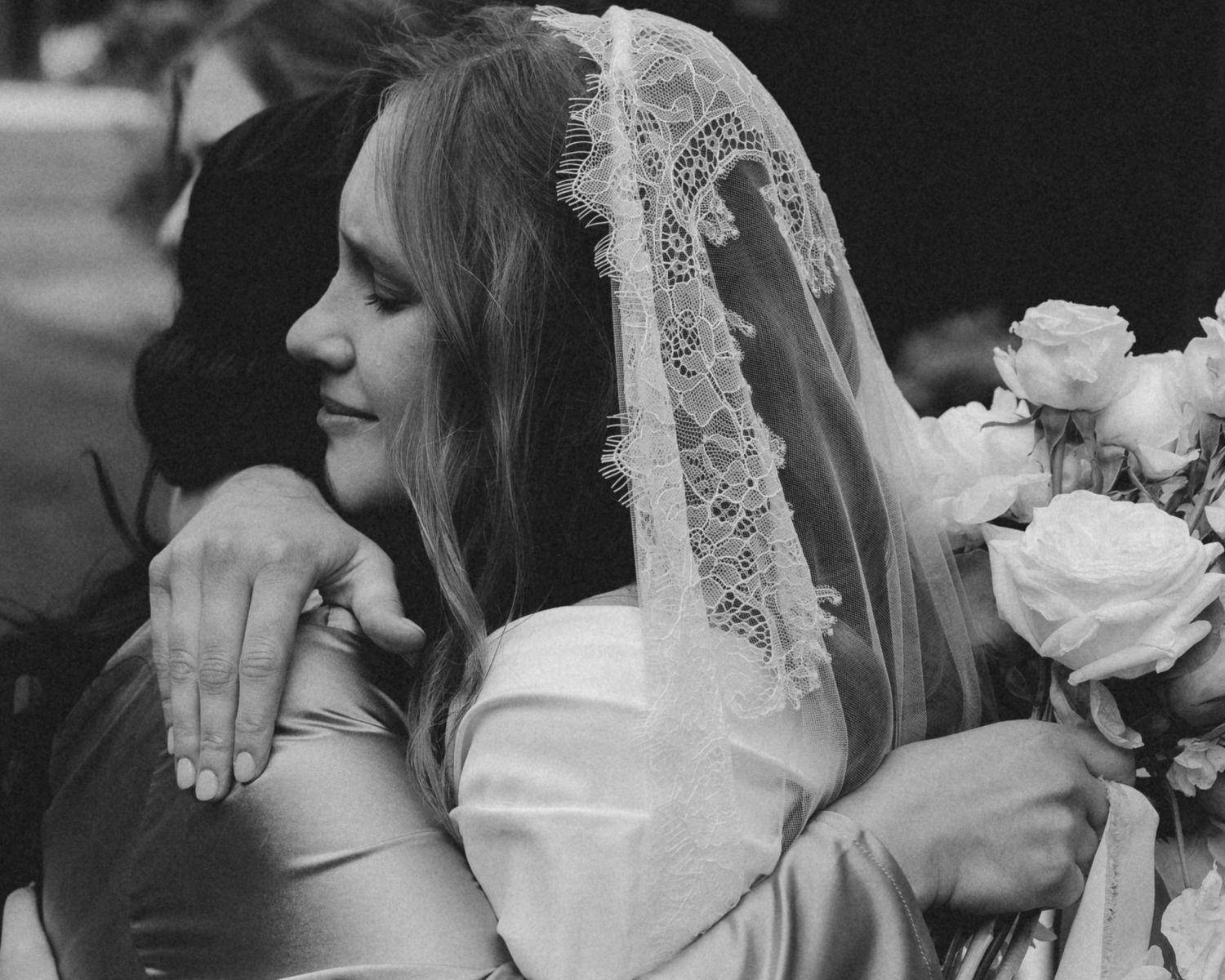 A black and white wedding photo showing a delicate lace veil and white roses in a romantic embrace.