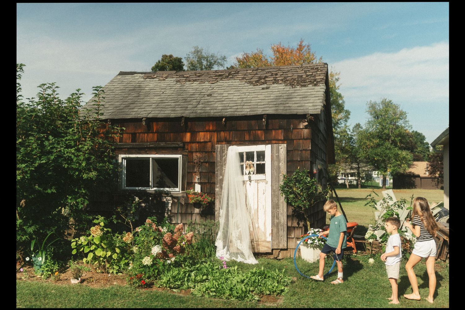 A rustic farmhouse with a weathered wooden exterior sits nestled among trees and greenery in a rural setting.