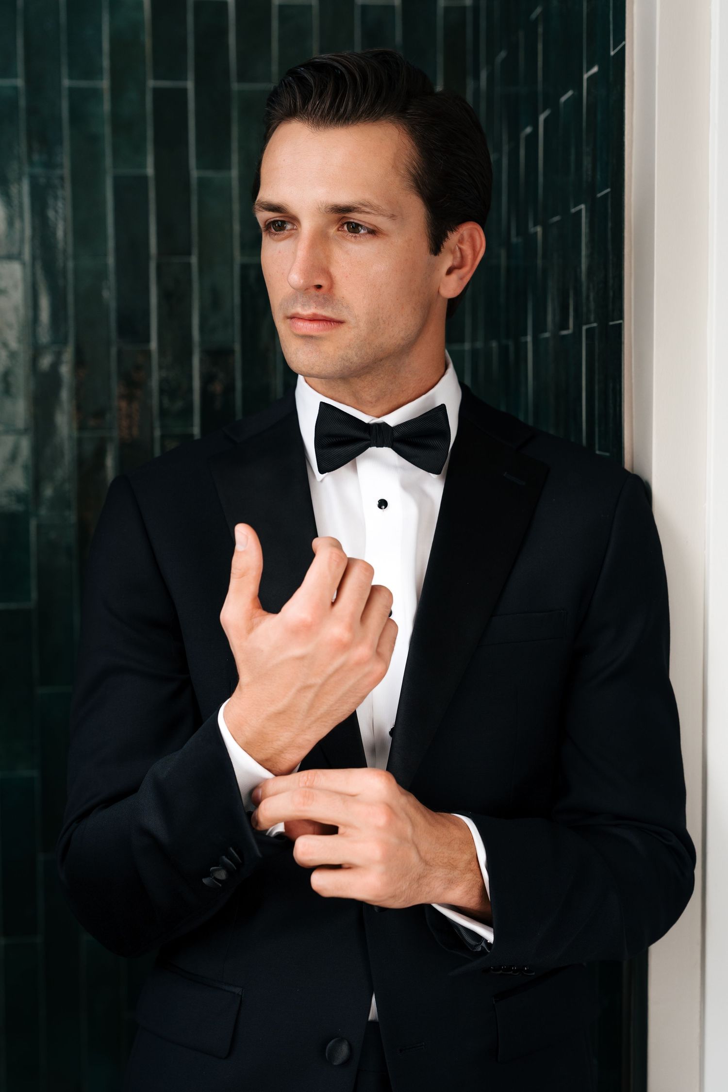 Close-up shots of a groom adjusting his bowtie and cuffs in a classic black tuxedo.