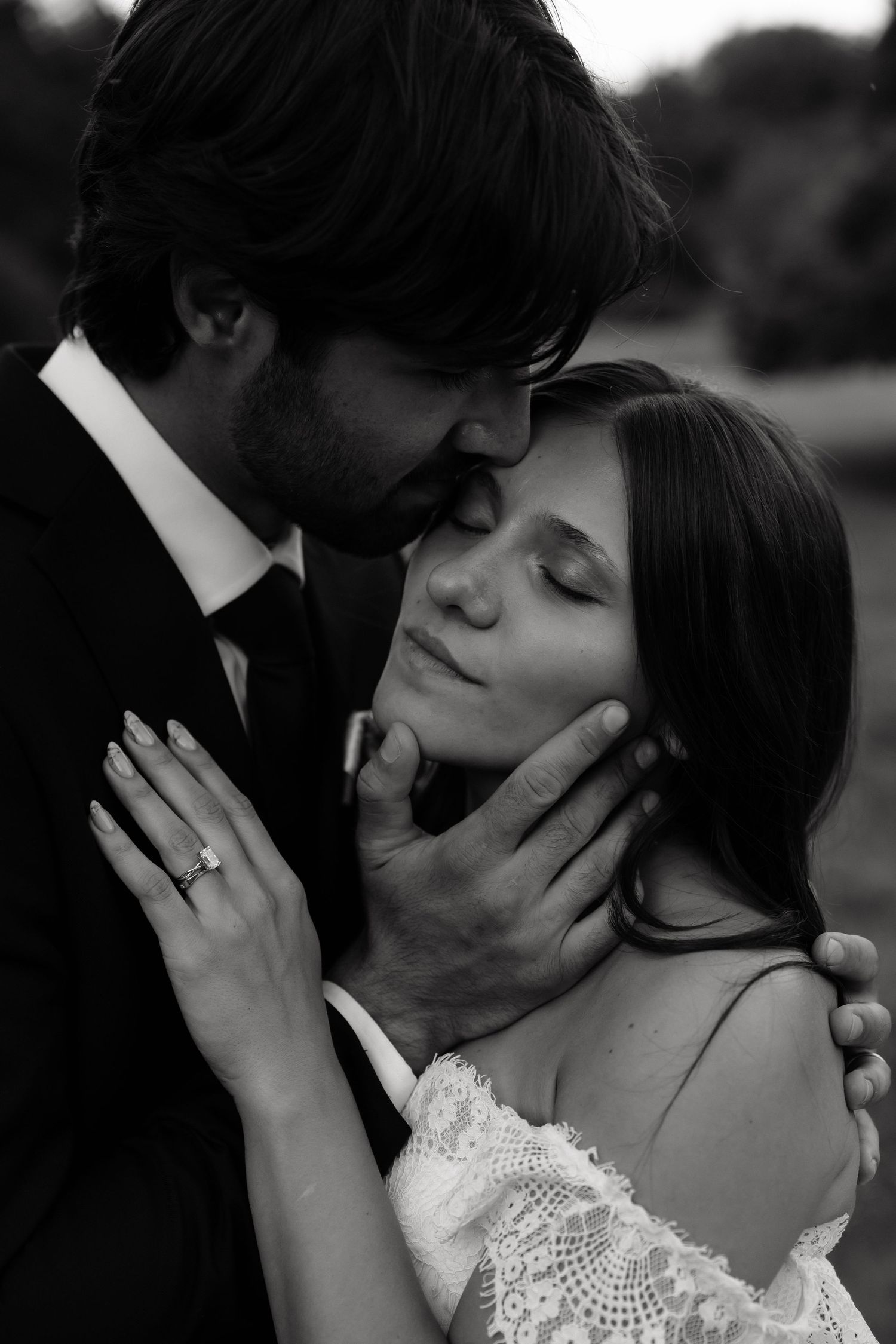 Intimate black and white close-up of groom tenderly holding brides face outdoors.