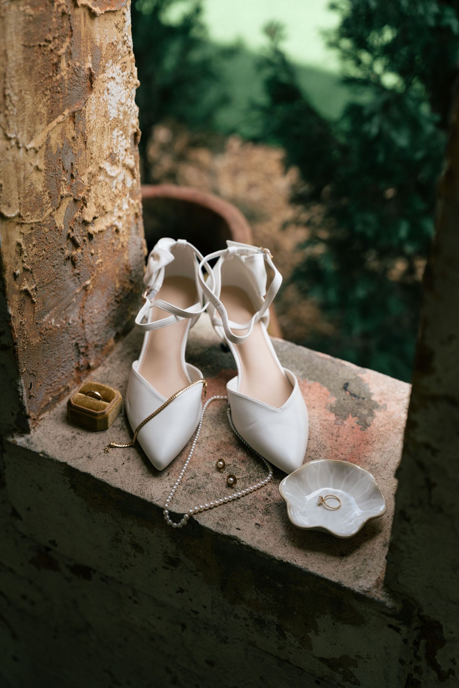 Elegant white bridal shoes with bows displayed on a rustic stone ledge in artistic composition.