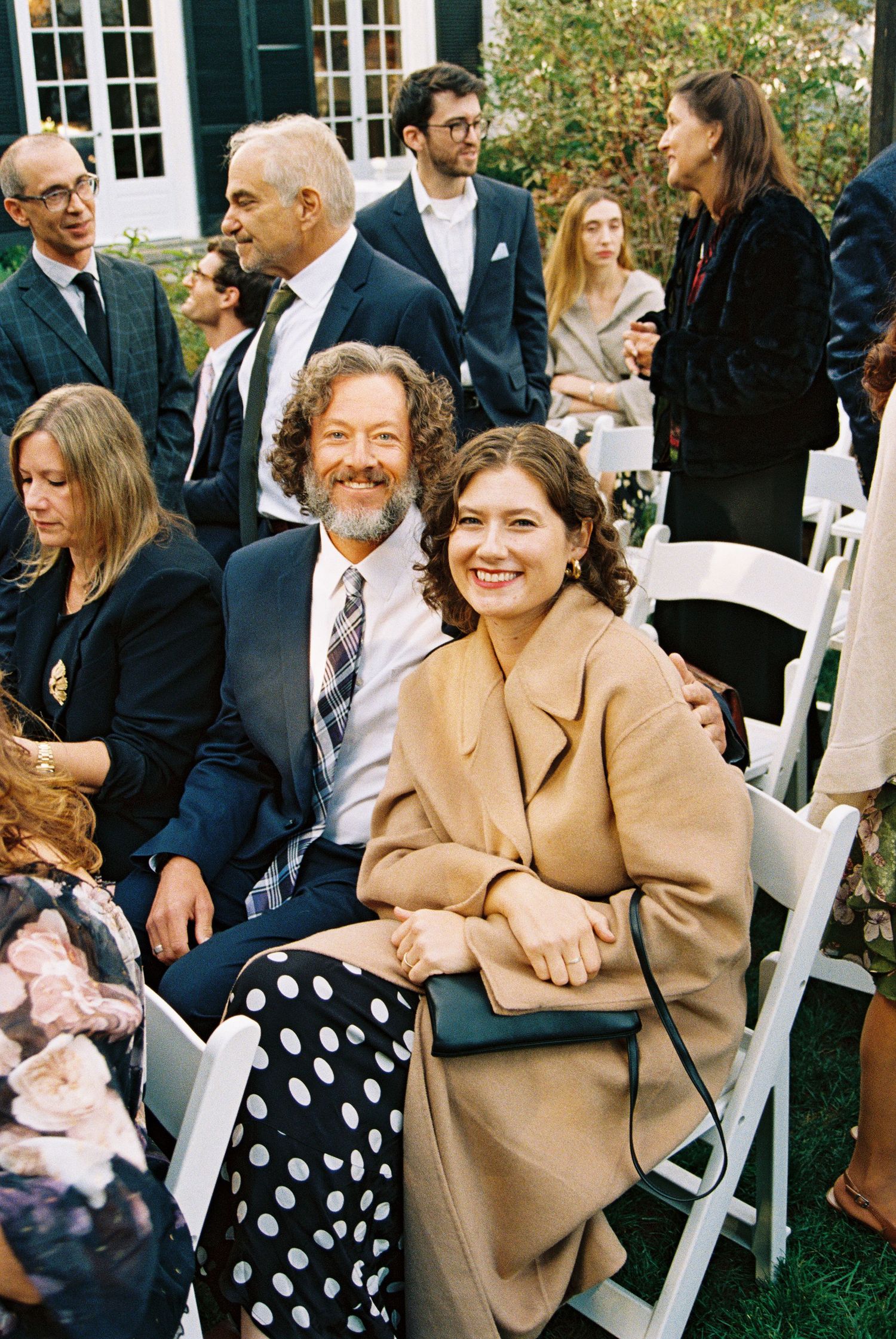 Wedding guests seated in white chairs during an outdoor garden ceremony.