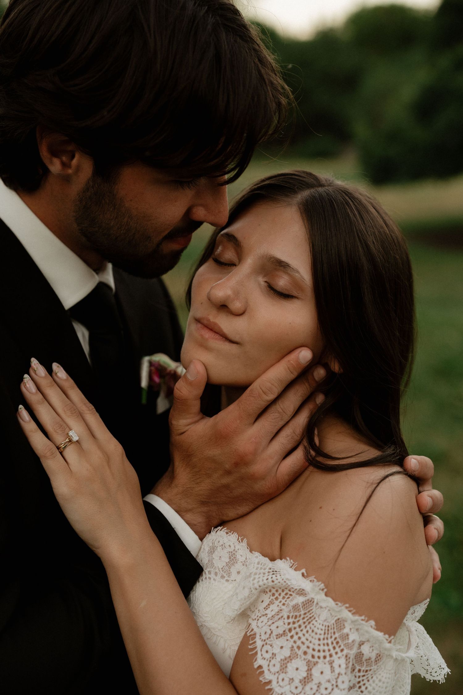 Groom tenderly holds brides face as she closes her eyes in an intimate wedding portrait outdoors.