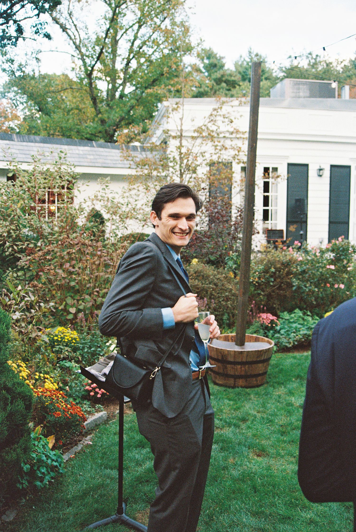 Groomsmen in dark suits prepare in a garden setting with flowering plants and barrels.