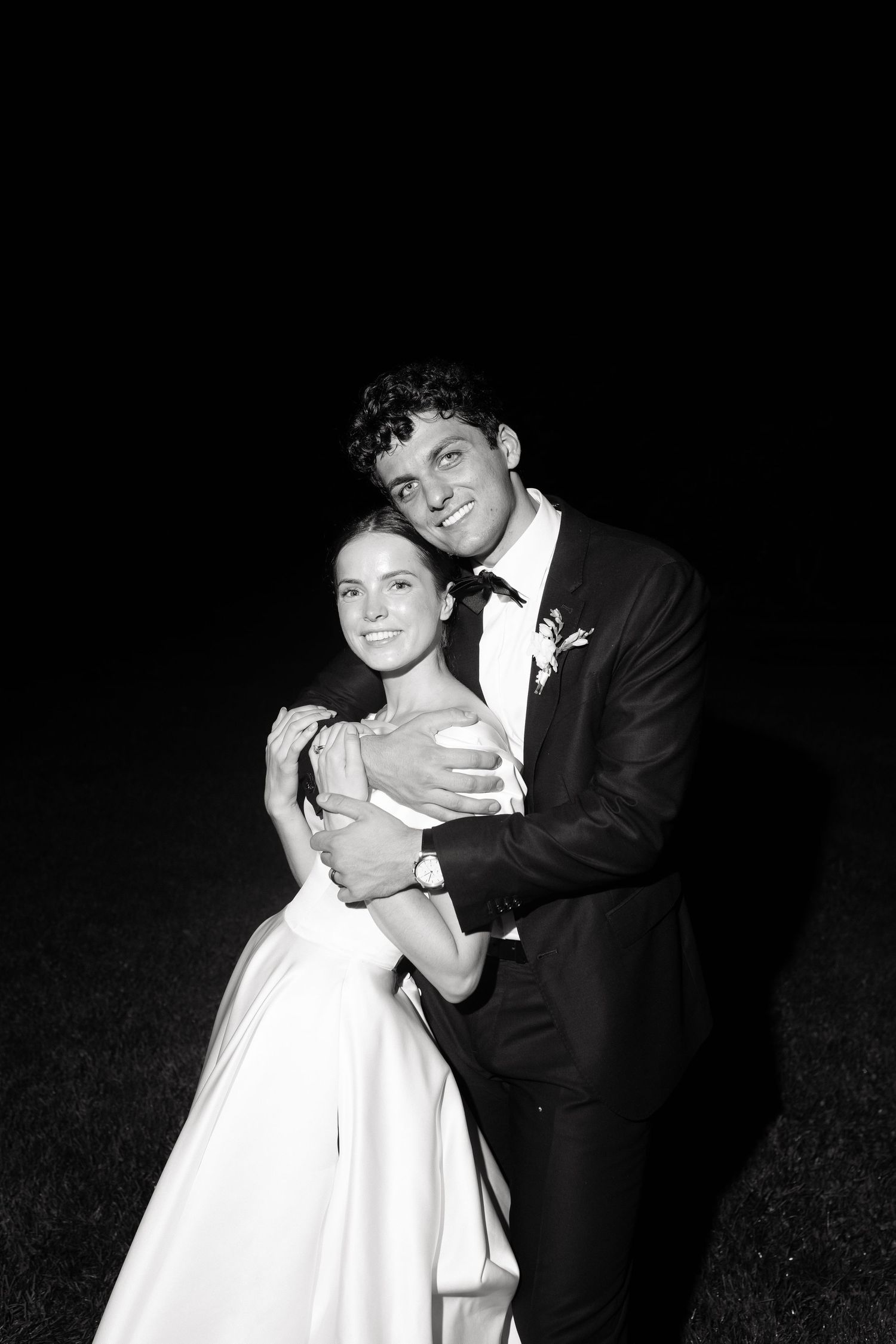 A black and white portrait of a couple embracing during their wedding celebration at night.