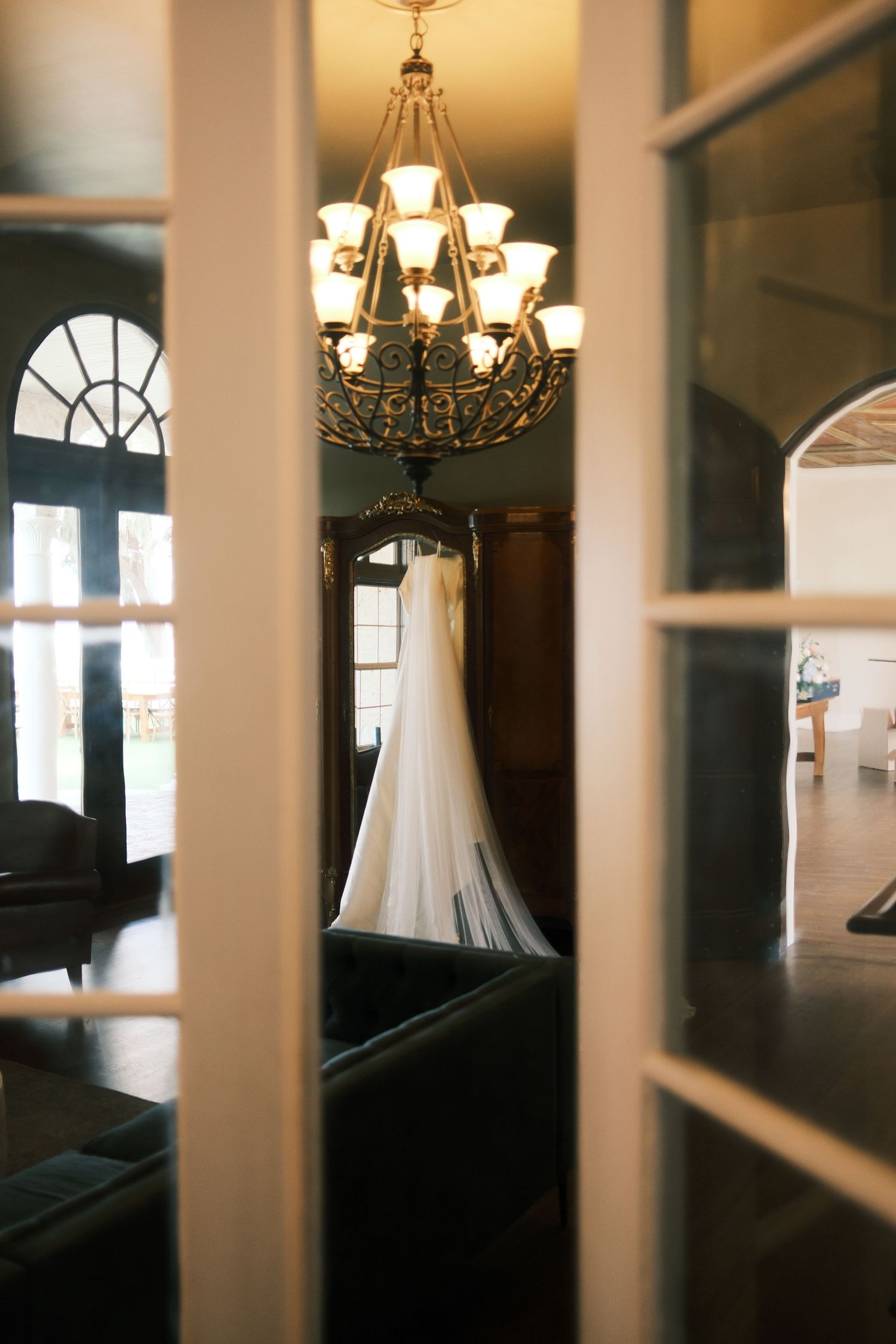 Elegant chandeliers and arched windows seen through architectural columns in an interior space.
