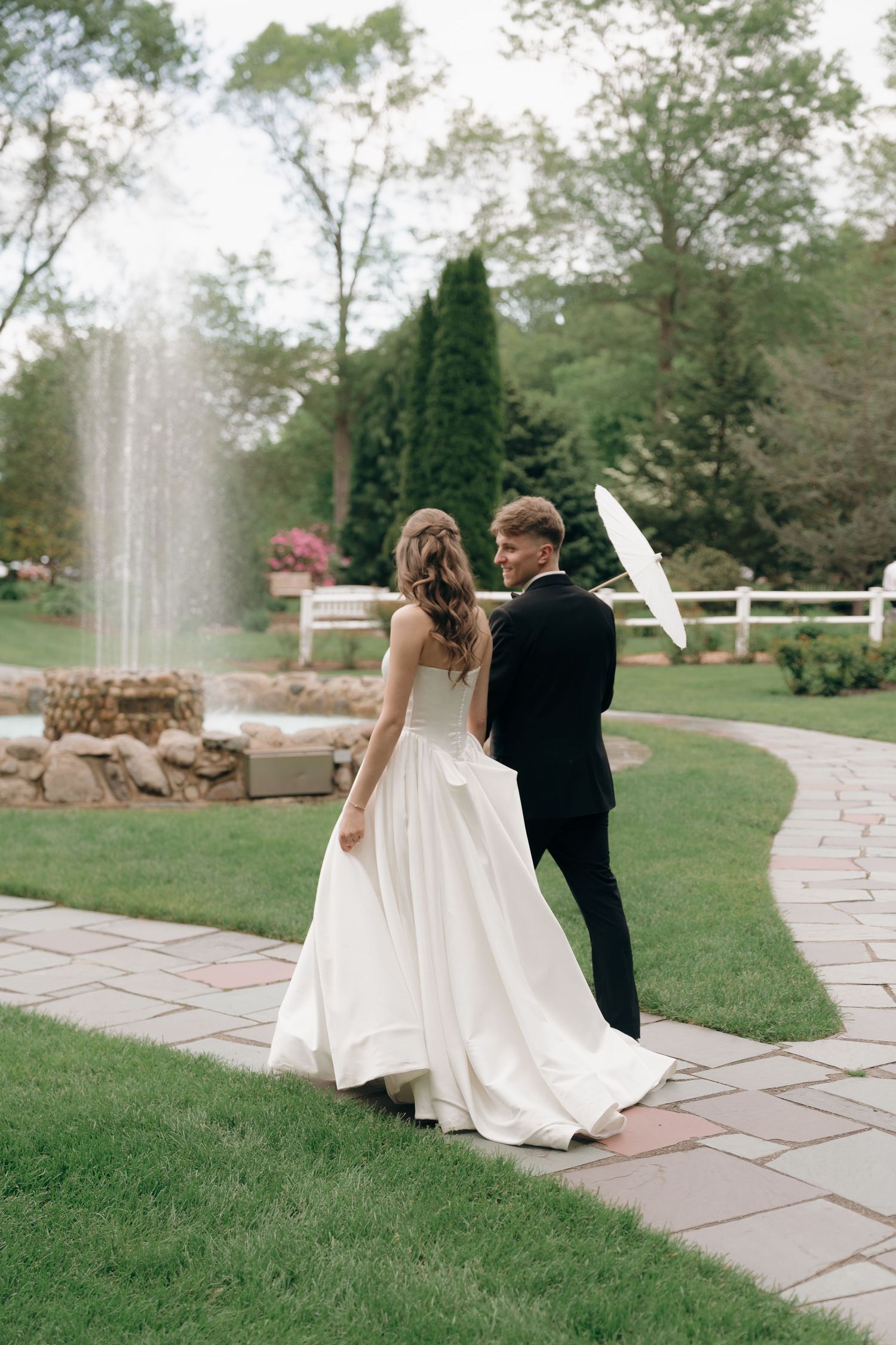 A romantic wedding couple walks along a stone path through a lush garden setting on their special day.