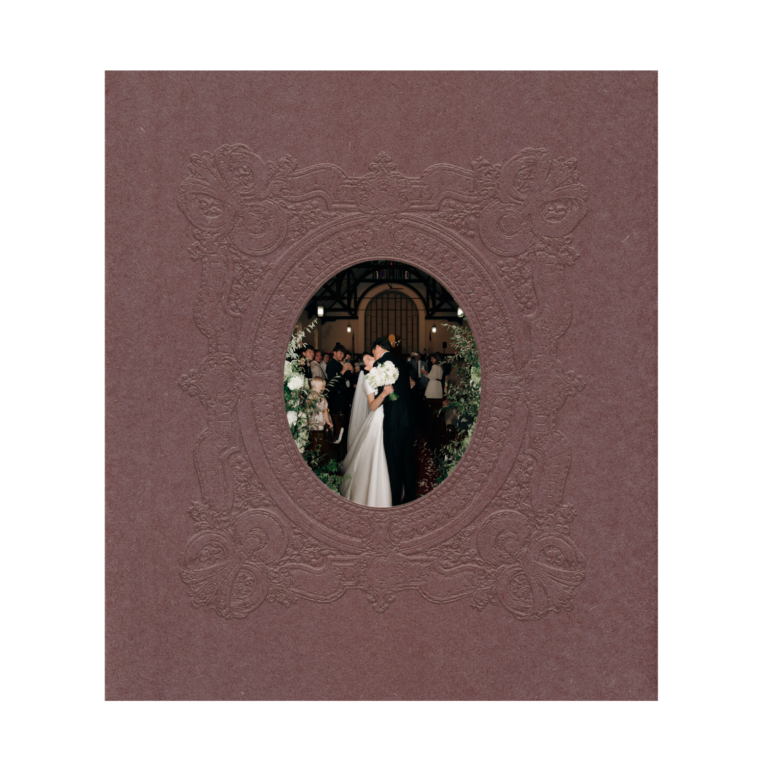 Brown embossed wedding photo album with oval window showcasing bride and groom at floral ceremony entrance.