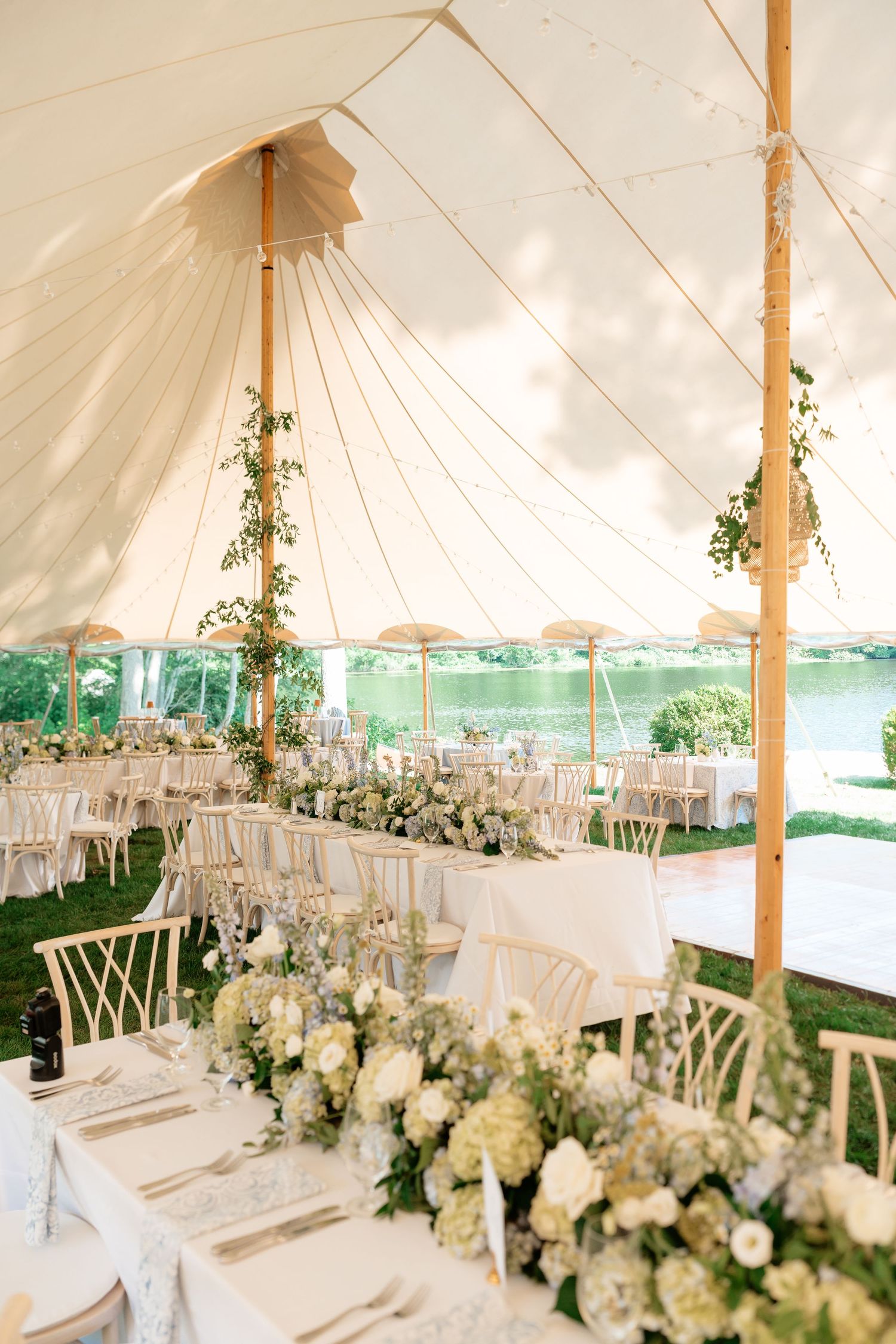 Elegant outdoor wedding reception under a white tent with floral centerpieces, white chairs, and waterfront views.