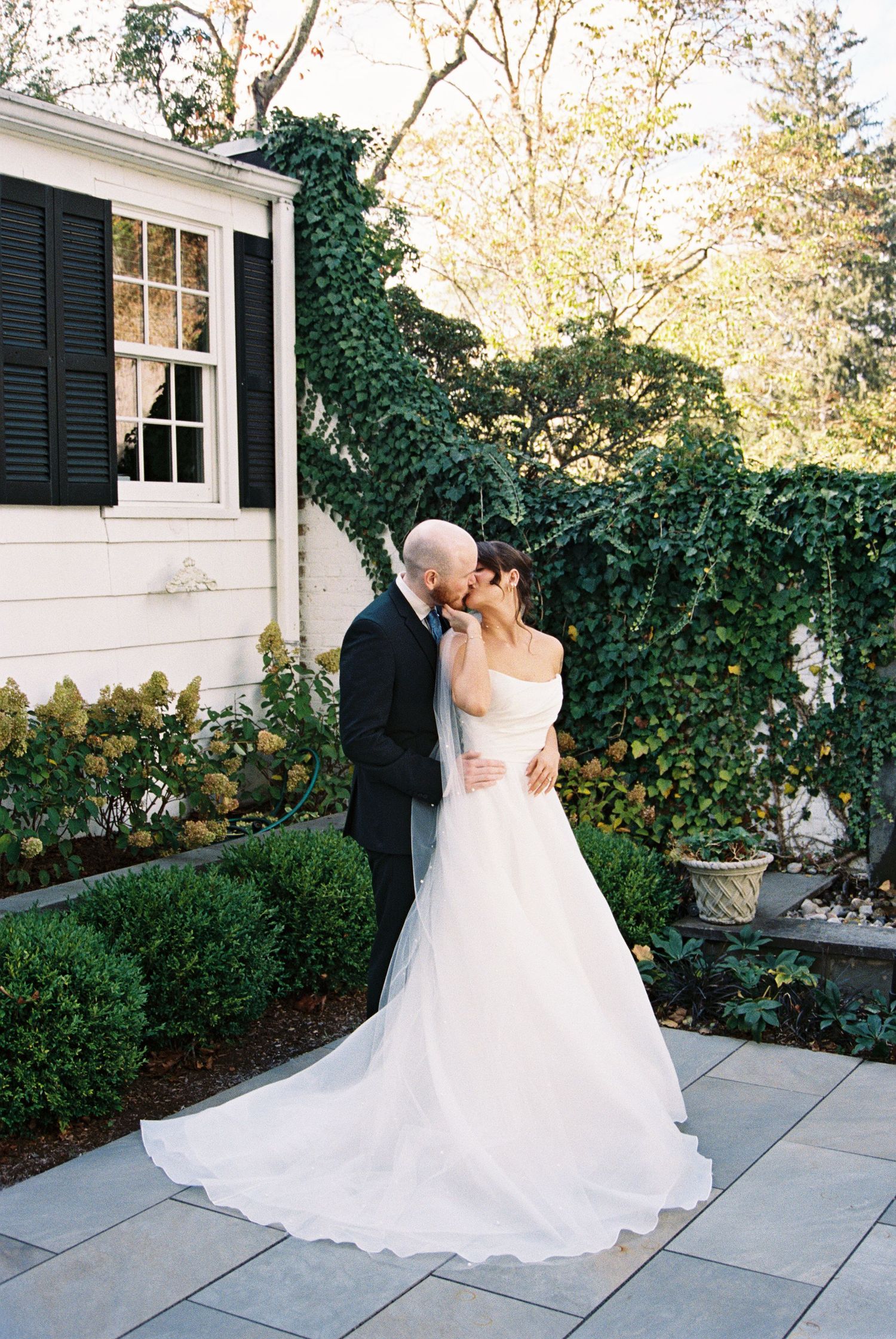 A romantic wedding moment captured outside a white colonial style house with ivy covered walls.