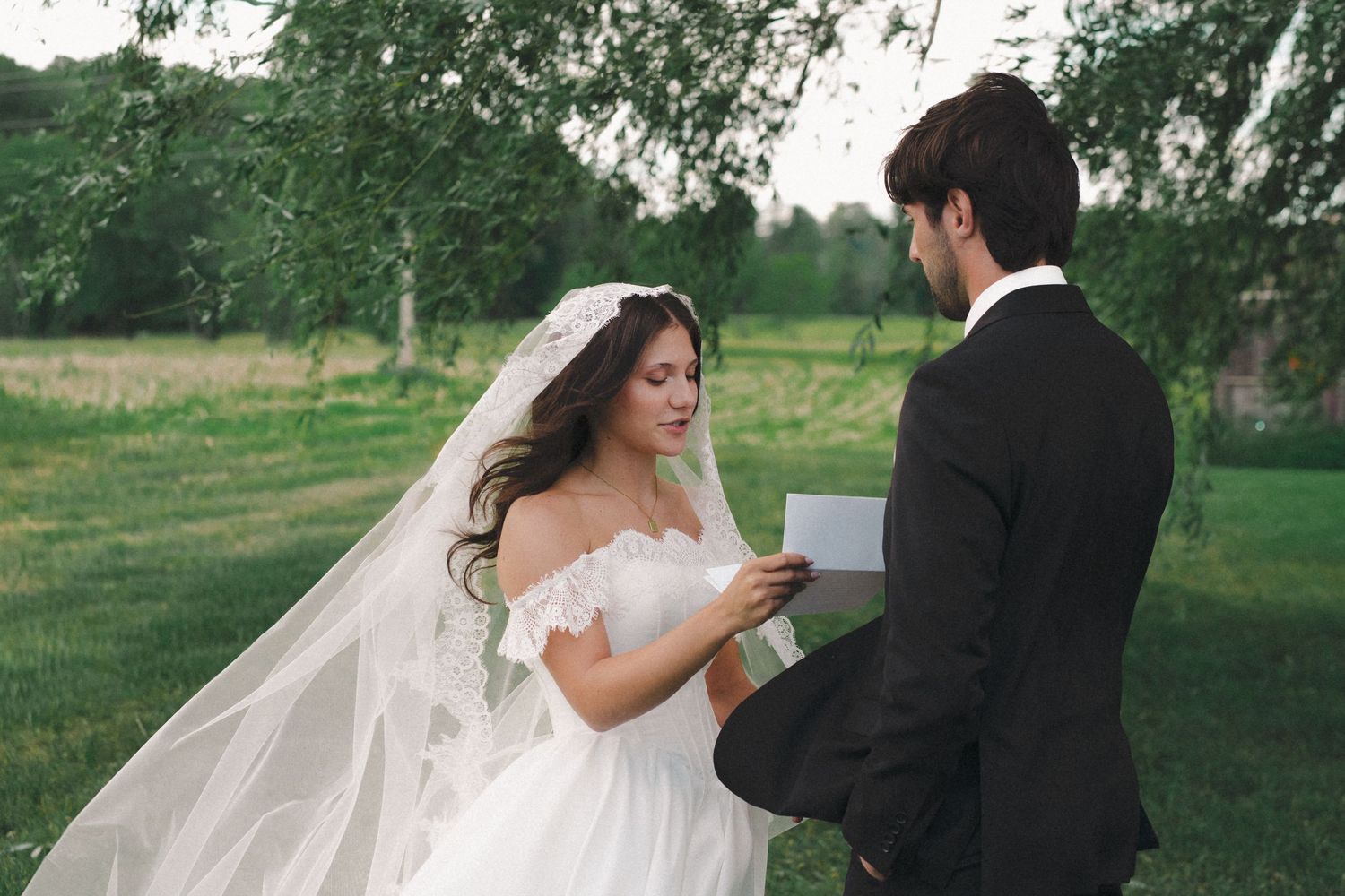 Bride and groom exchange vows outdoors in a lush green garden, bride wearing white gown and veil.