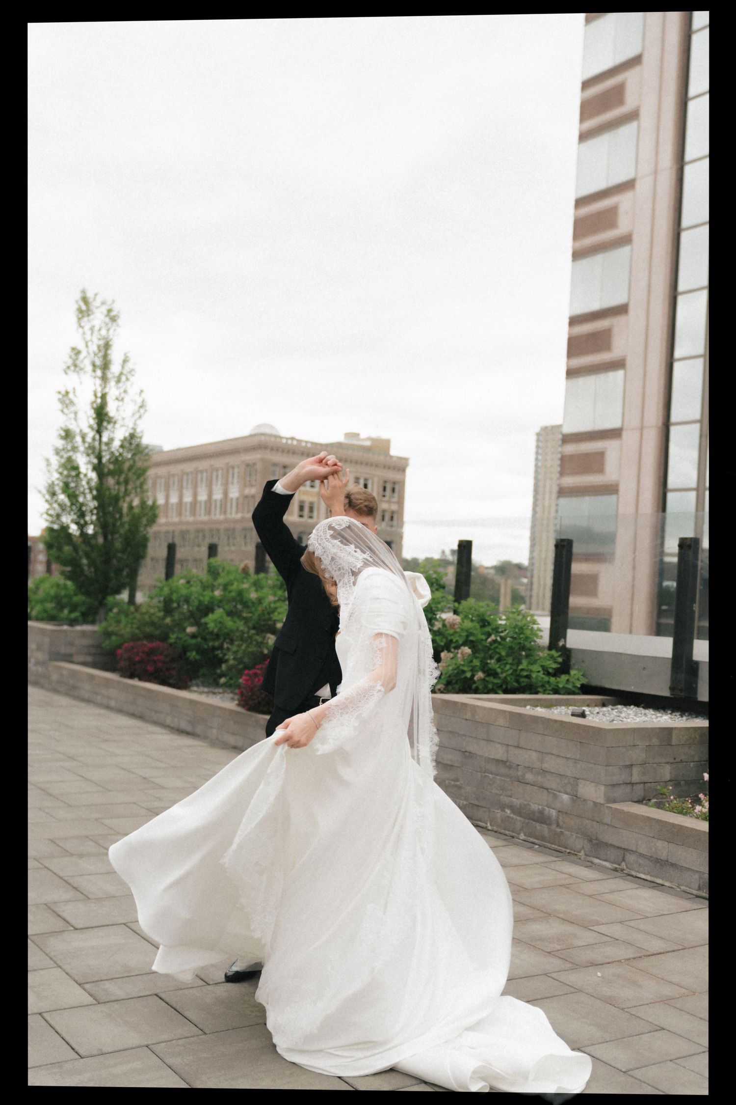 A flowing white wedding dress twirls gracefully against a modern architectural backdrop on a stone terrace.