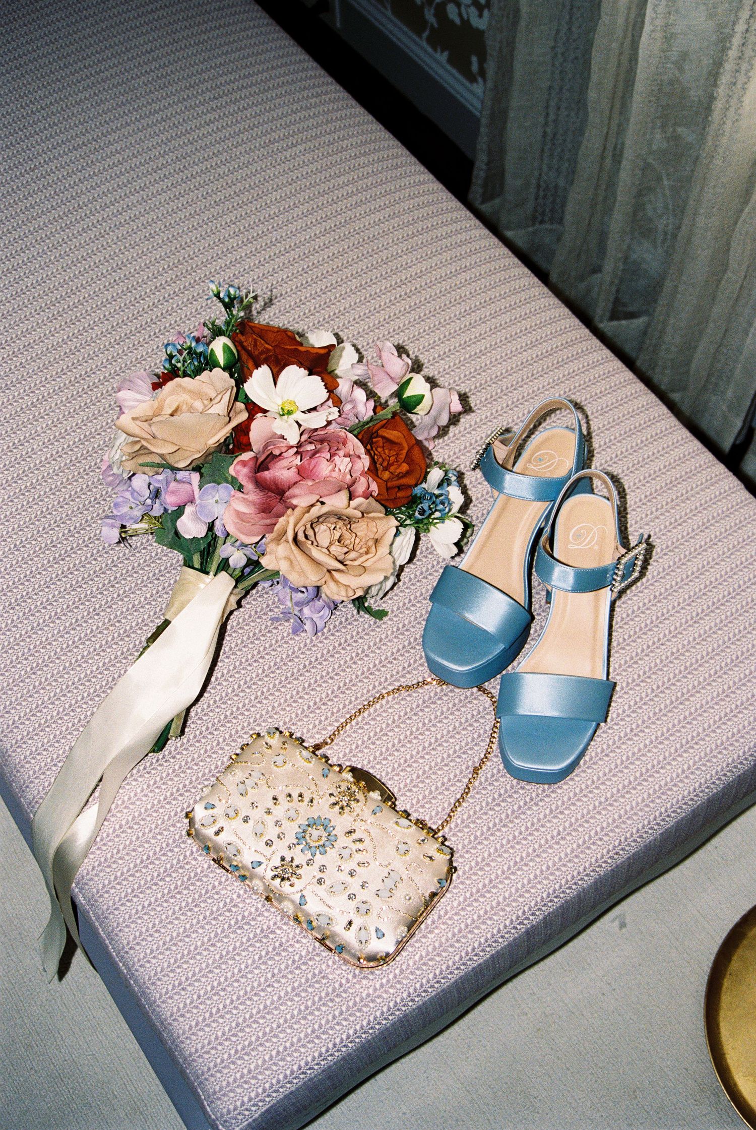 Wedding accessories including blue heels, floral crown, and delicate details arranged on textured surface.