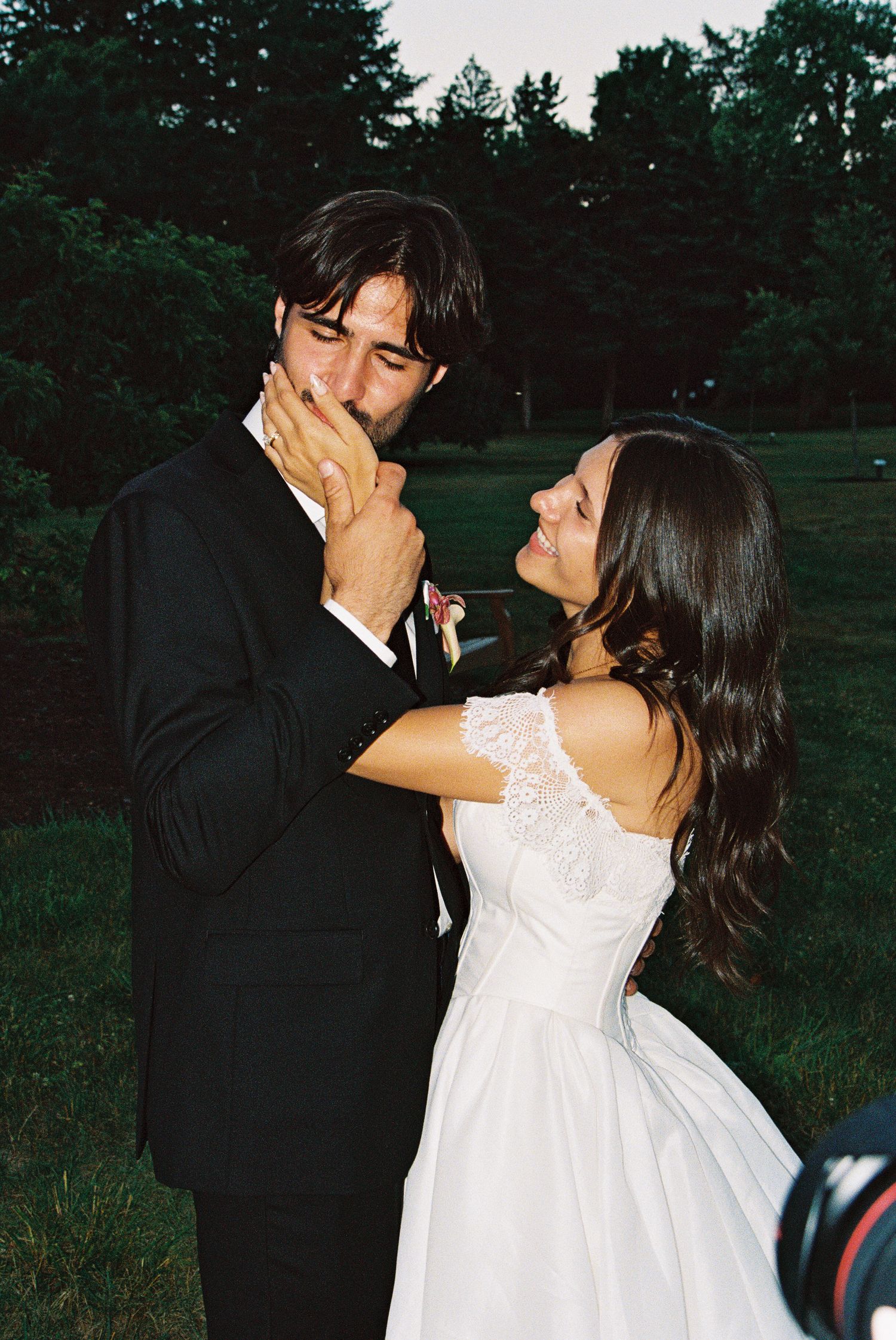 Bride and groom share an intimate moment outdoors, with the groom kissing her hand during their wedding celebration.