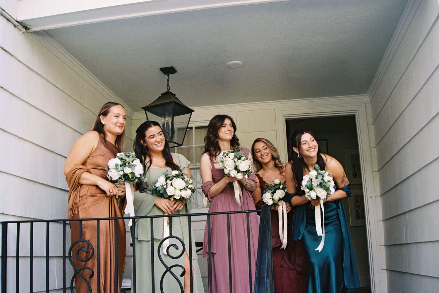 Bridesmaids in mixed colored dresses posing together on a covered porch.
