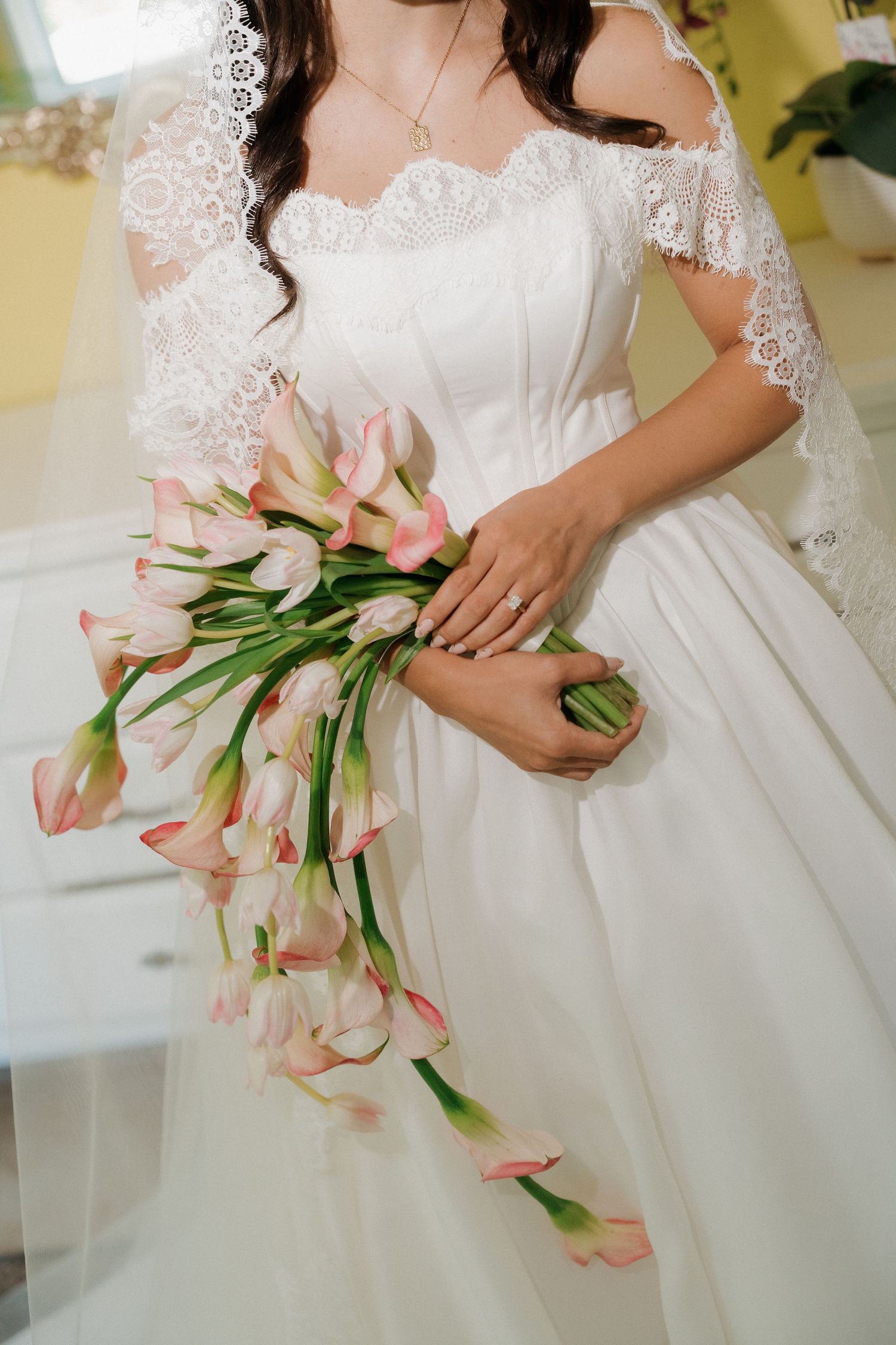 Bride in white lace off-shoulder gown holding a cascading bouquet of pink tulips on her wedding day.