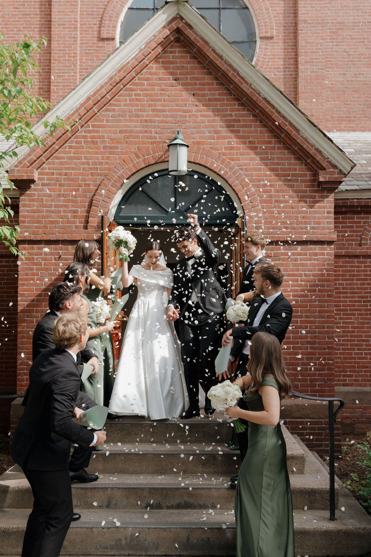 Wedding party celebrates with confetti outside a brick church entrance.