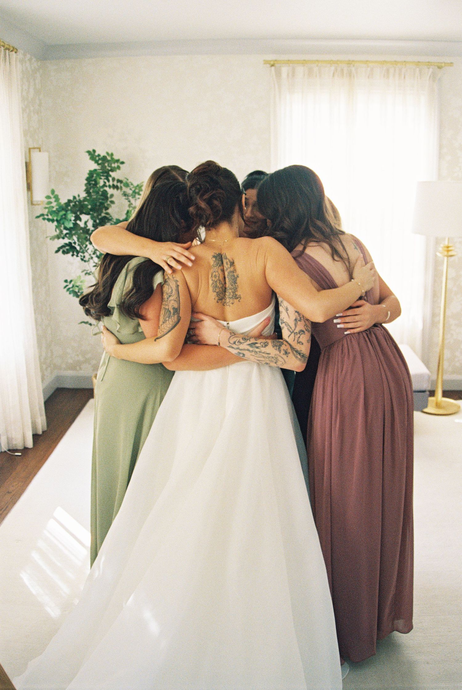 Bridesmaids in earth-toned dresses share an intimate group hug moment.