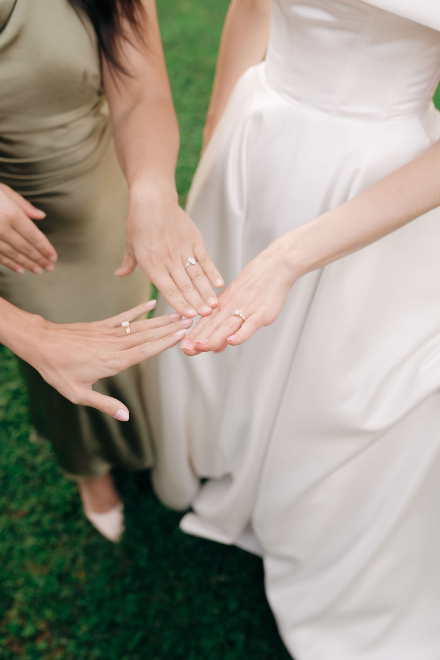 Hands tenderly hold the flowing fabric of a white wedding dress against a green outdoor background.