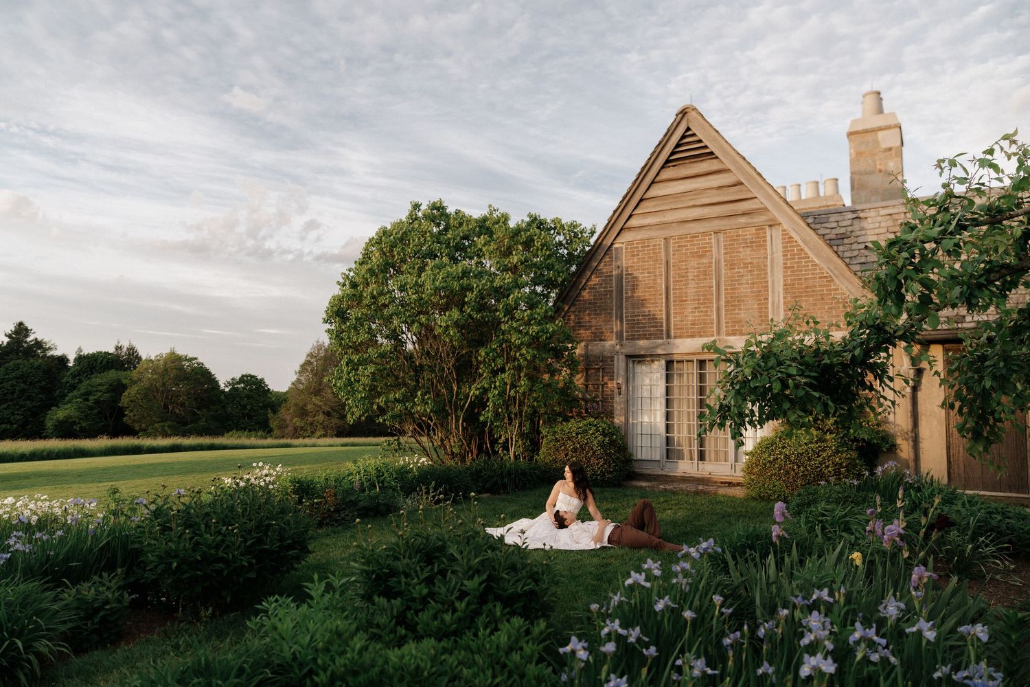 Woman meditating on a blanket in a lush garden beside a charming rustic wooden barn at golden hour.