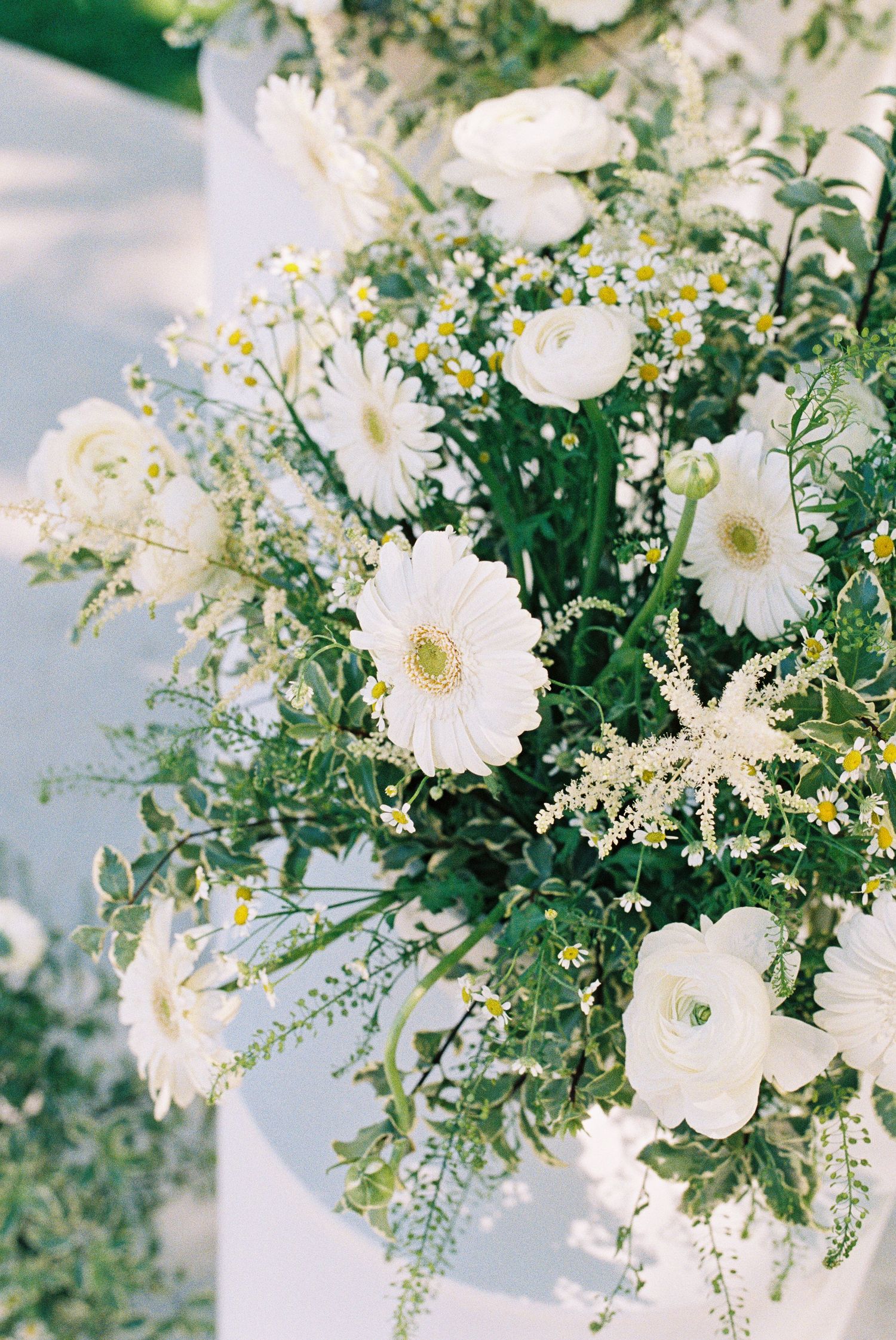 White gerbera daisies, ranunculus, and wildflowers arranged in a lush green floral bouquet for a wedding ceremony.