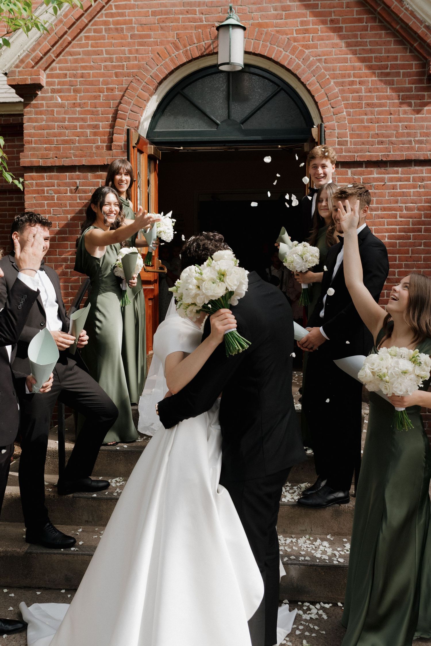 Joyful wedding celebration with confetti toss in front of a red brick church.