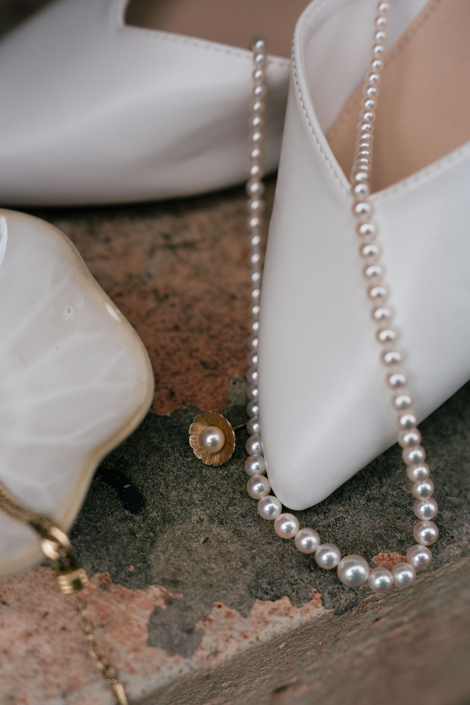 A delicate string of white pearl beads lies alongside flowing white fabric against a textured stone surface.