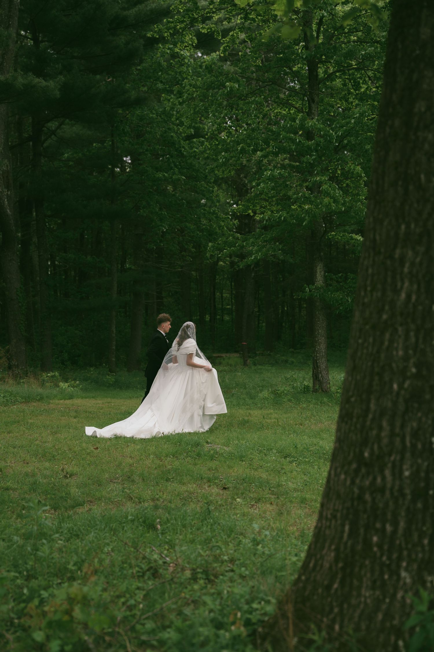 A wedding couple poses in a serene forest setting with lush green trees creating a romantic woodland backdrop.