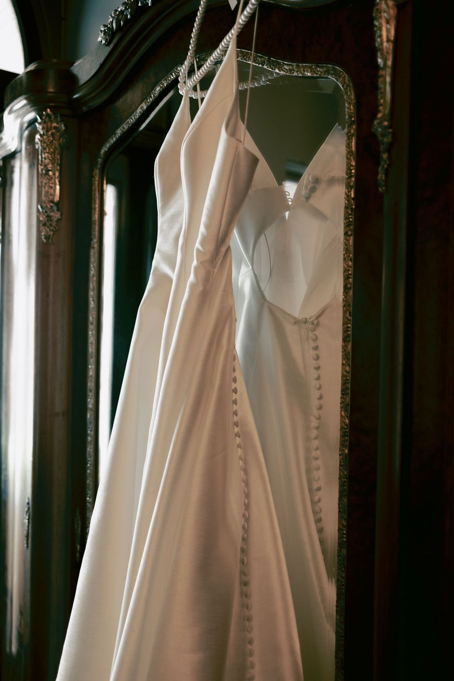 White wedding dresses hanging on display in a dimly lit room with elegant lighting and ornate details.
