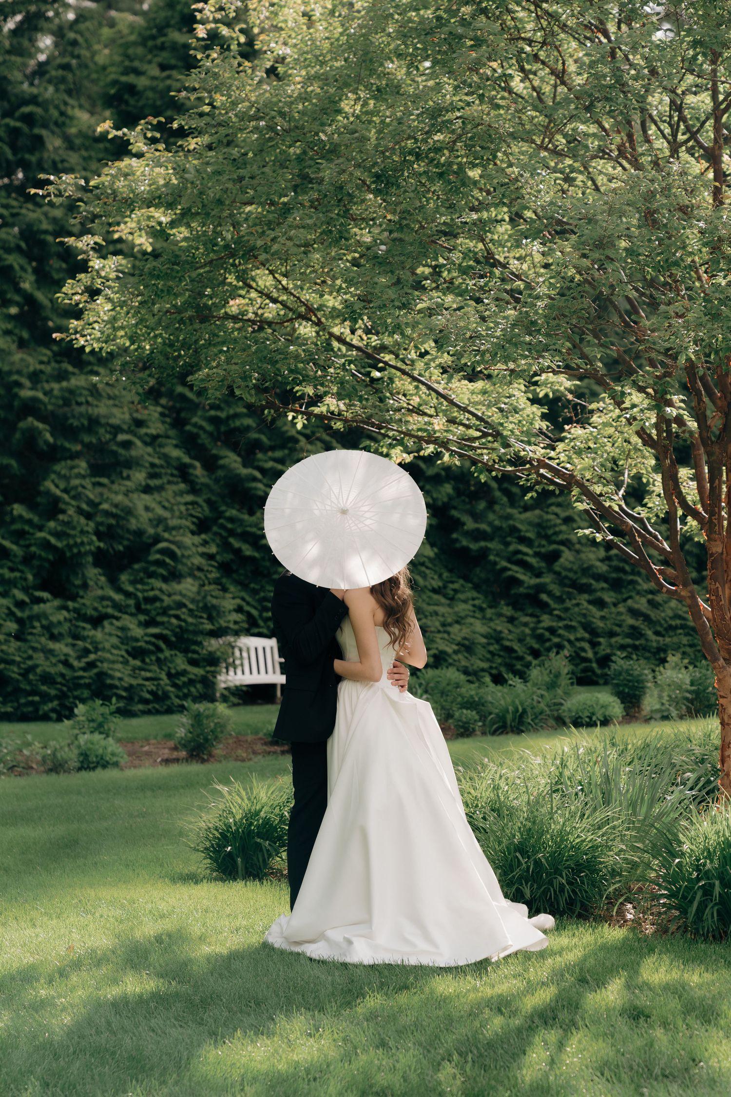 A white wedding dress is displayed against lush green garden scenery in a series of artistic shots.