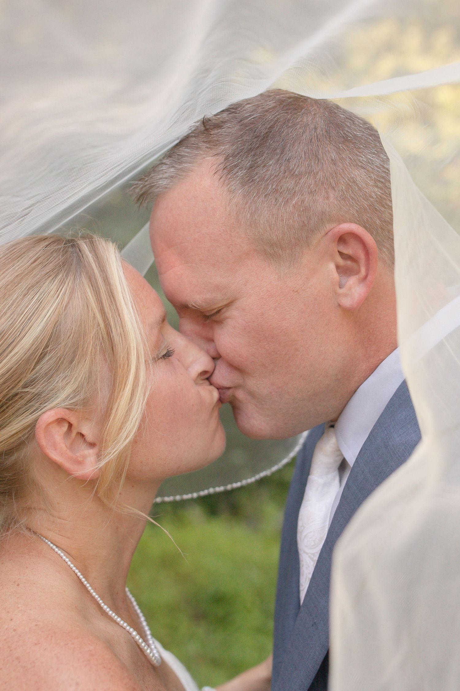 Romantic wedding kiss sequence between newlyweds under a flowing white veil against a natural backdrop.