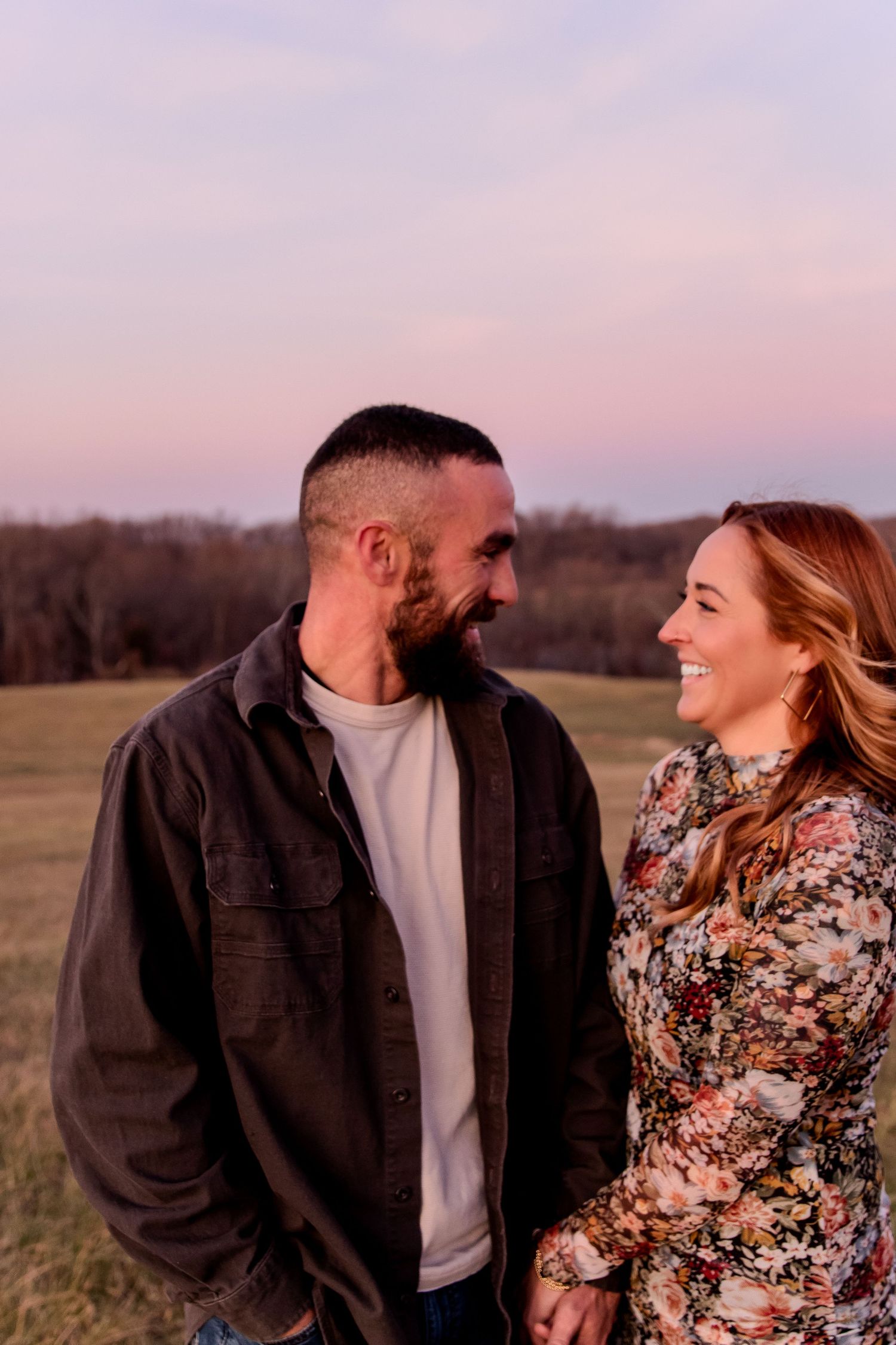 Romantic couple laughing together in a field during sunset while wearing cozy fall outfits.