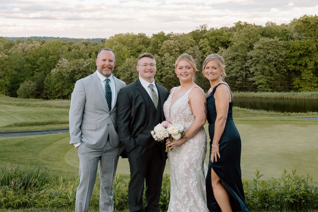 Wedding party members in formal attire gather on lush green golf course for outdoor portraits.