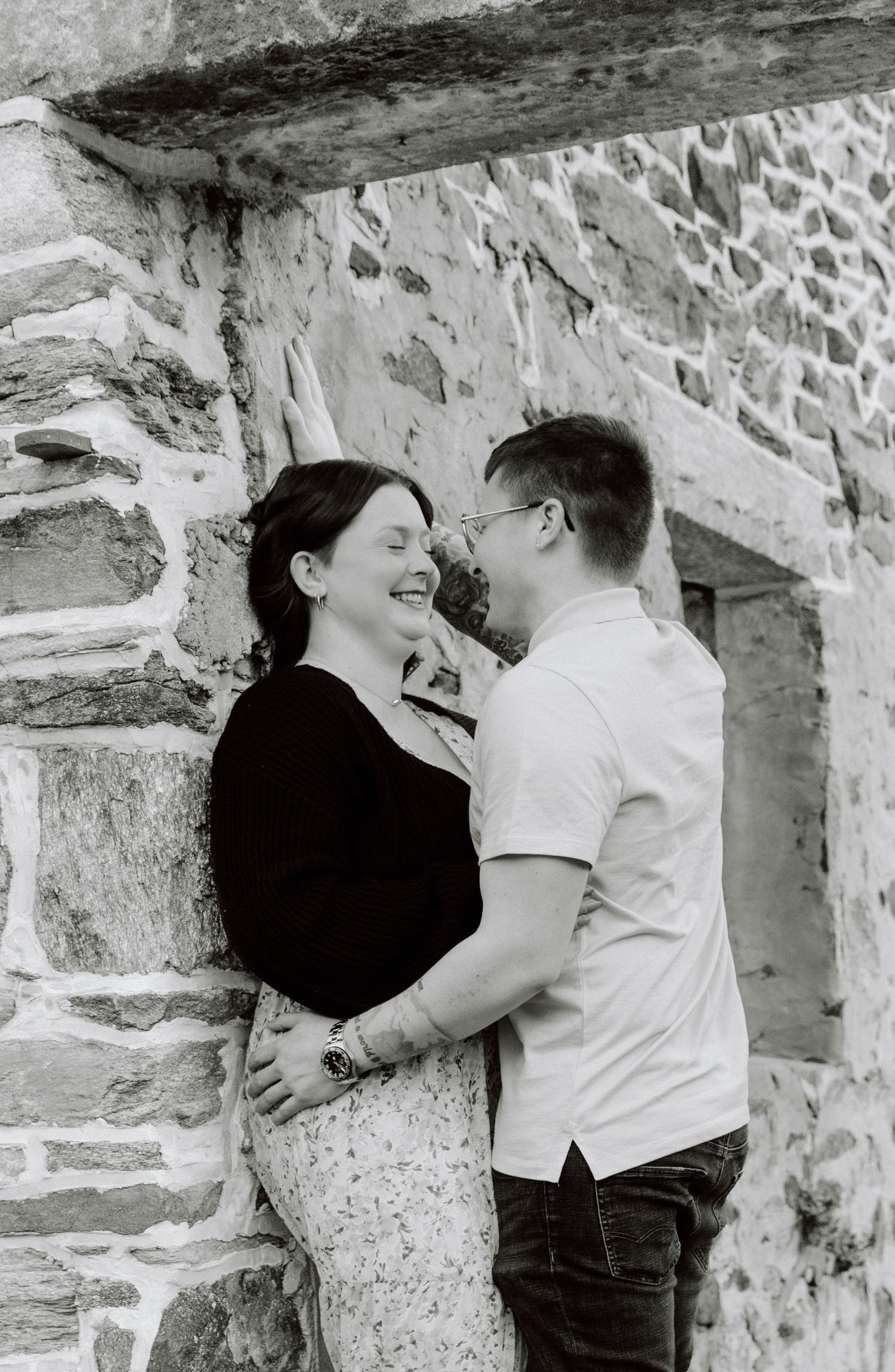 A romantic black and white portrait of a couple sharing an intimate moment against a stone wall background.