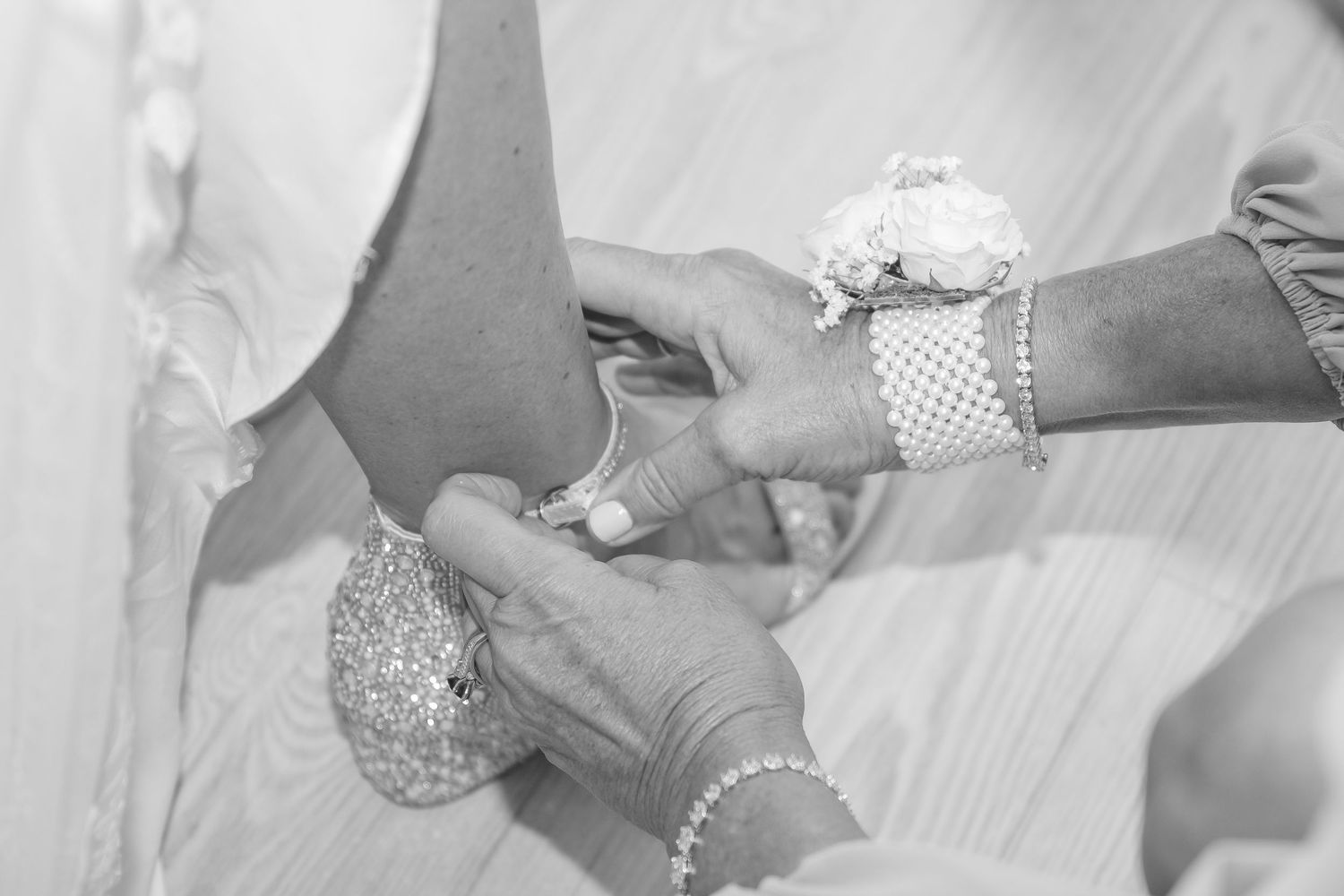 Hands placing a corsage or boutonniere on a guest's wrist at a formal special event.
