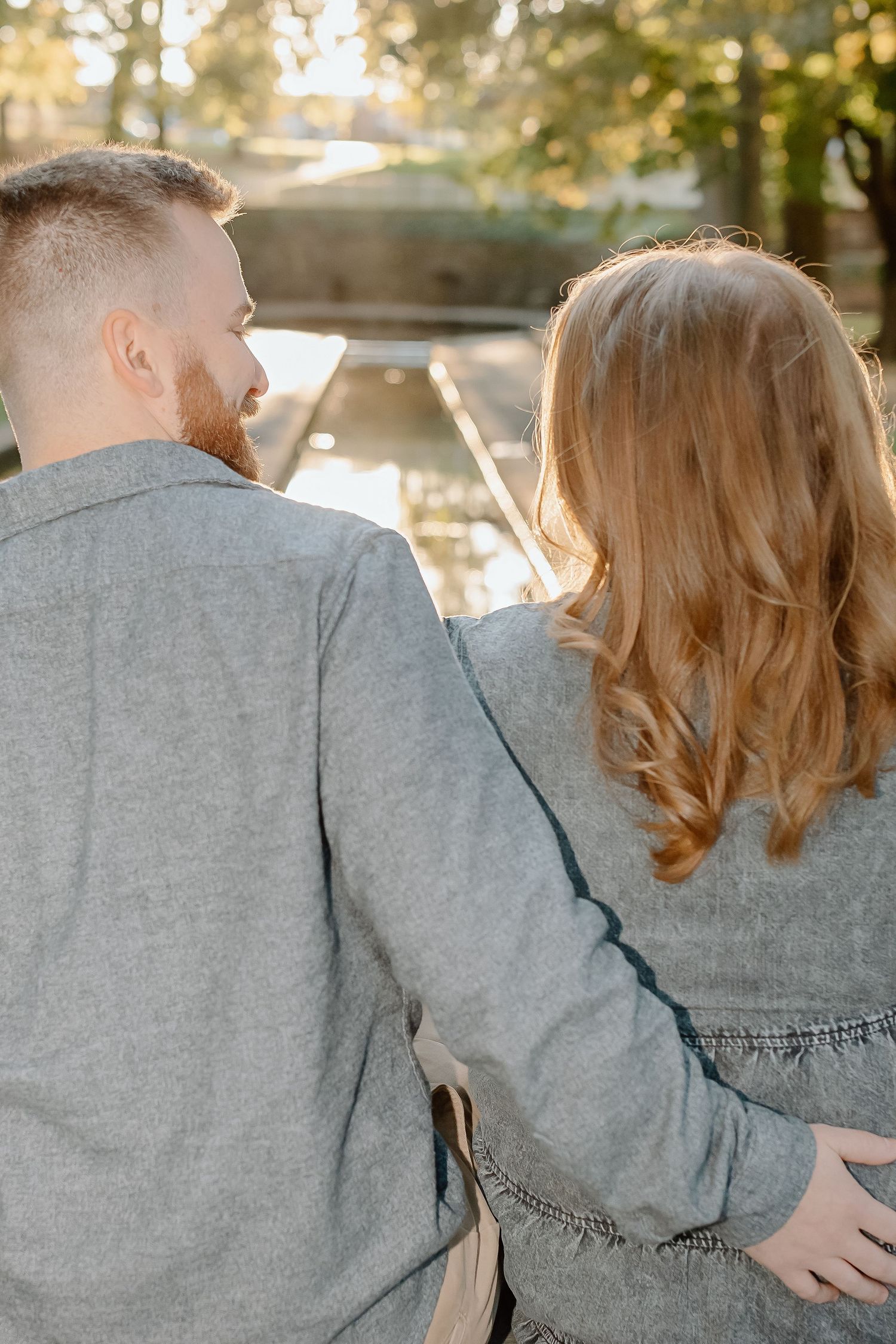A couple in matching grey outfits embraces while sitting outdoors during golden hour.