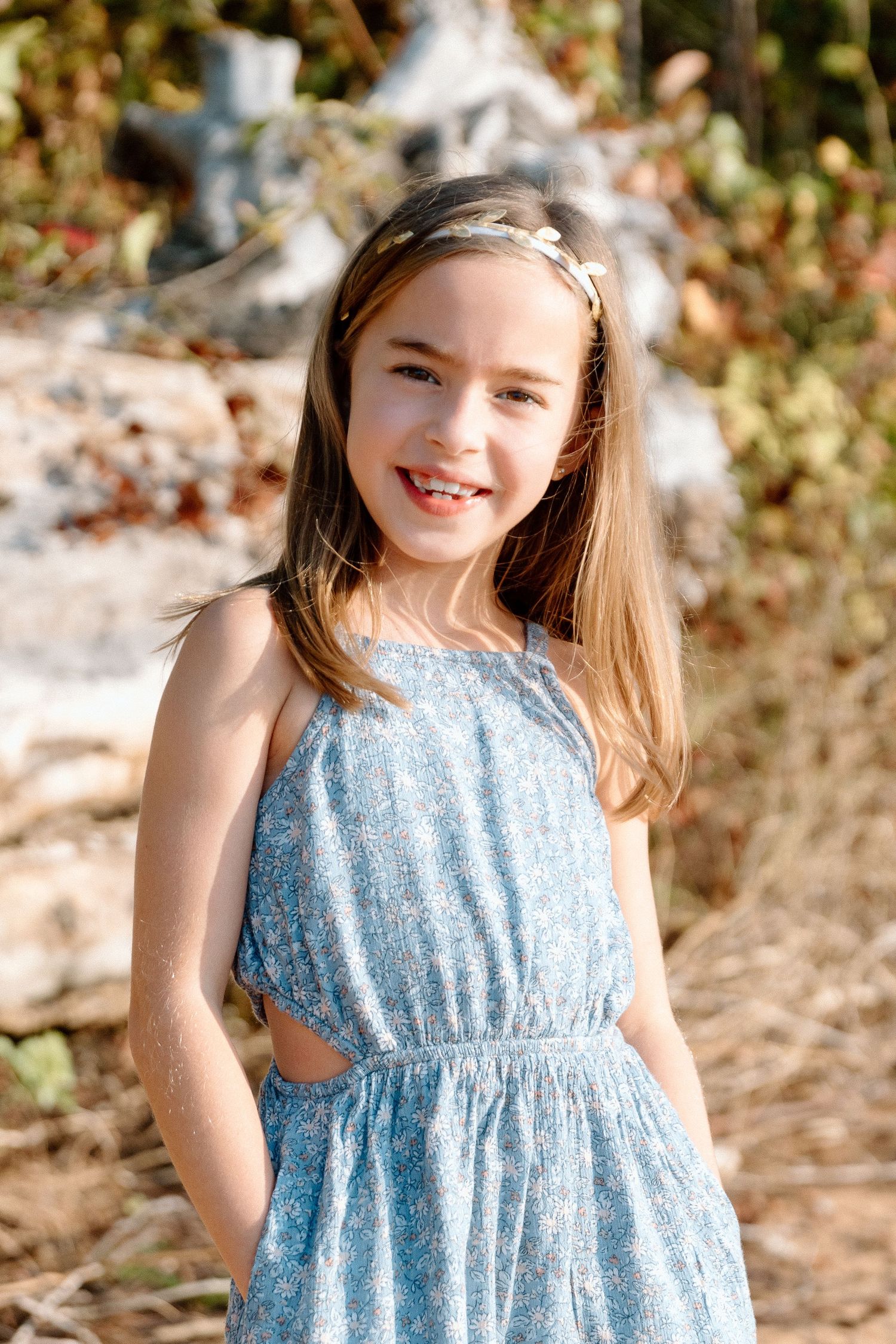 A child in a light blue floral dress twirls and smiles on a sunny day outdoors.