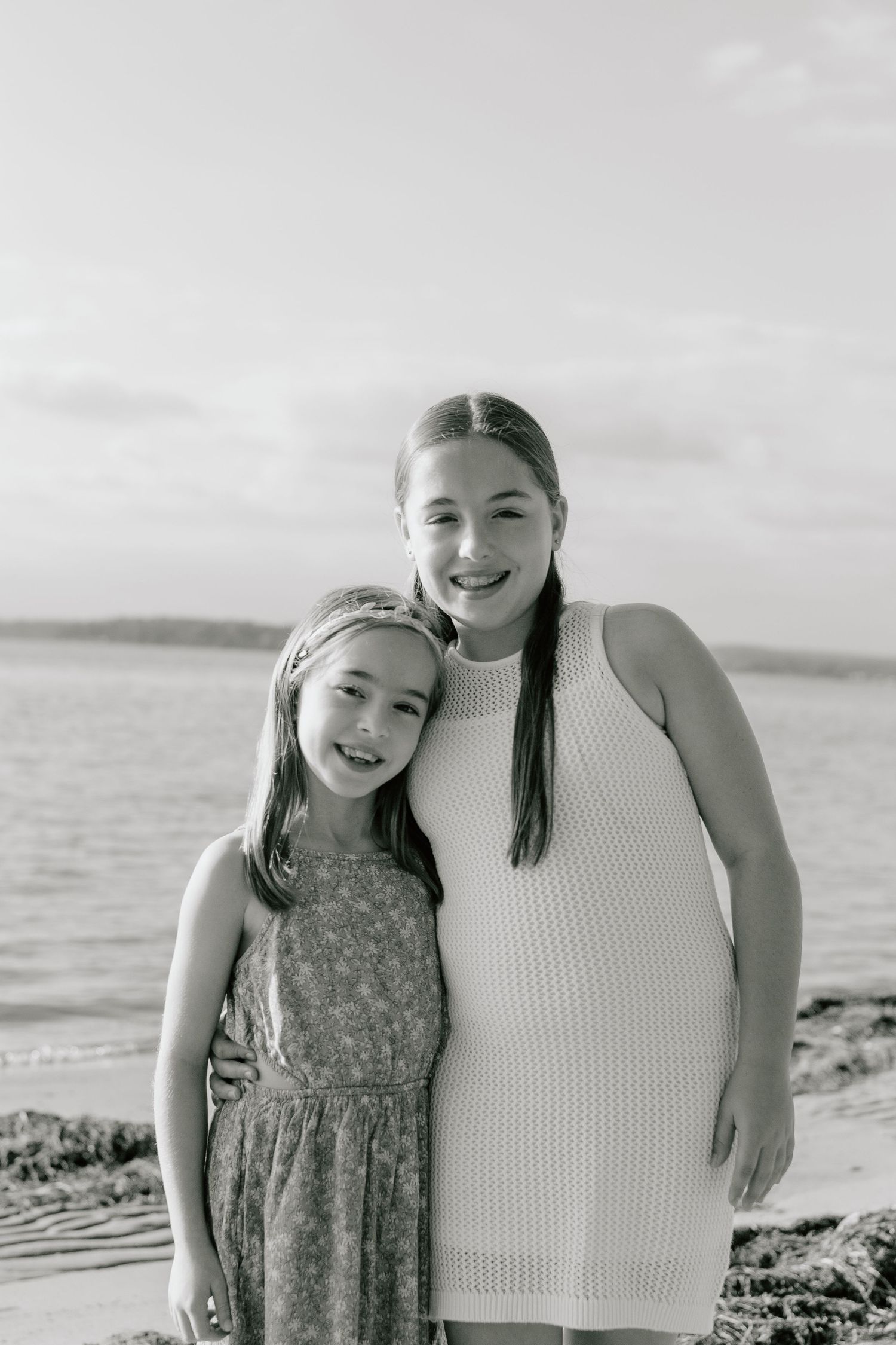 Mother and daughter posing together on a sunny beach in casual summer attire.