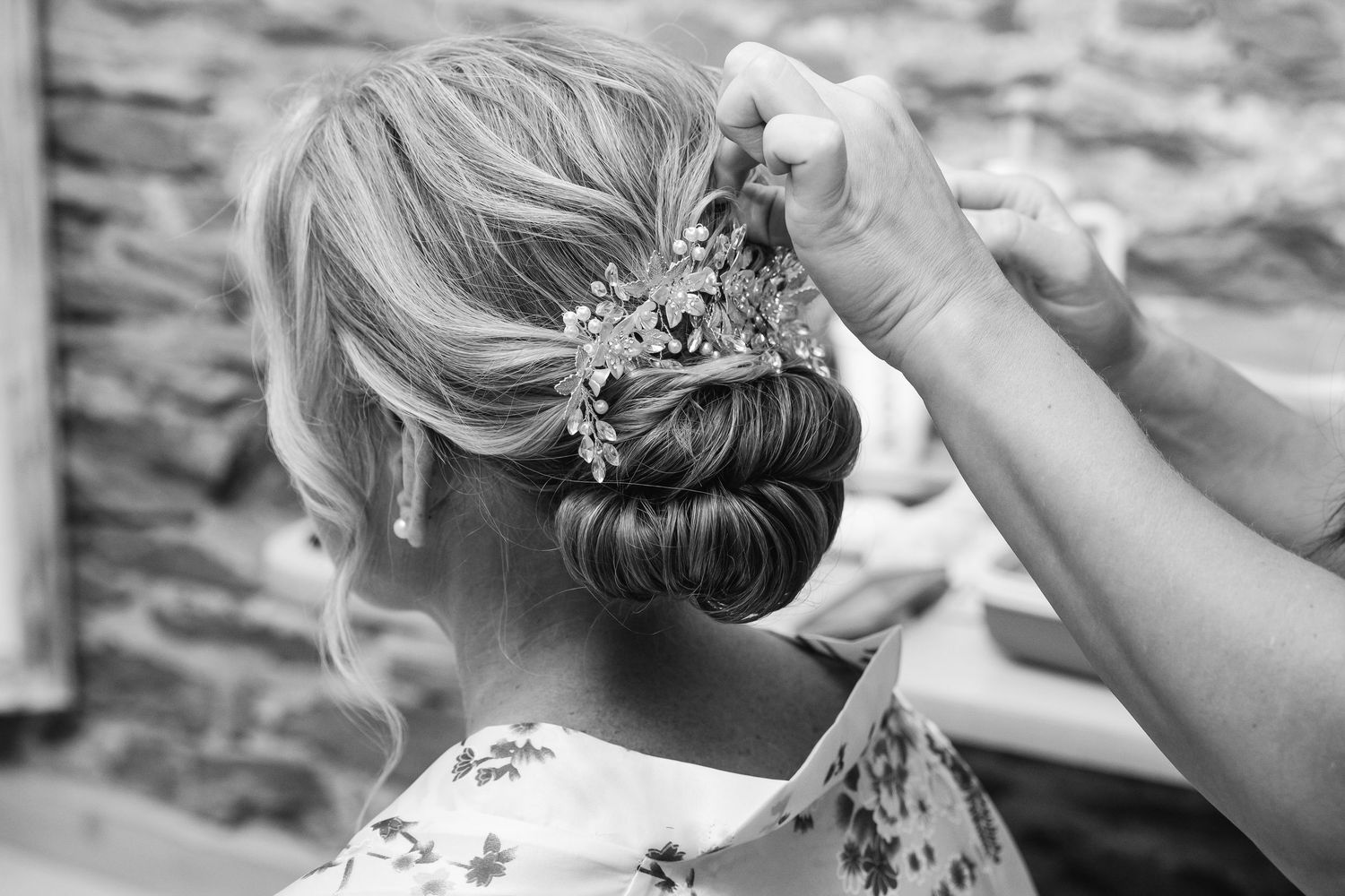 A hairstylist arranges an elegant updo with delicate floral accessories for a bridal hairstyle.