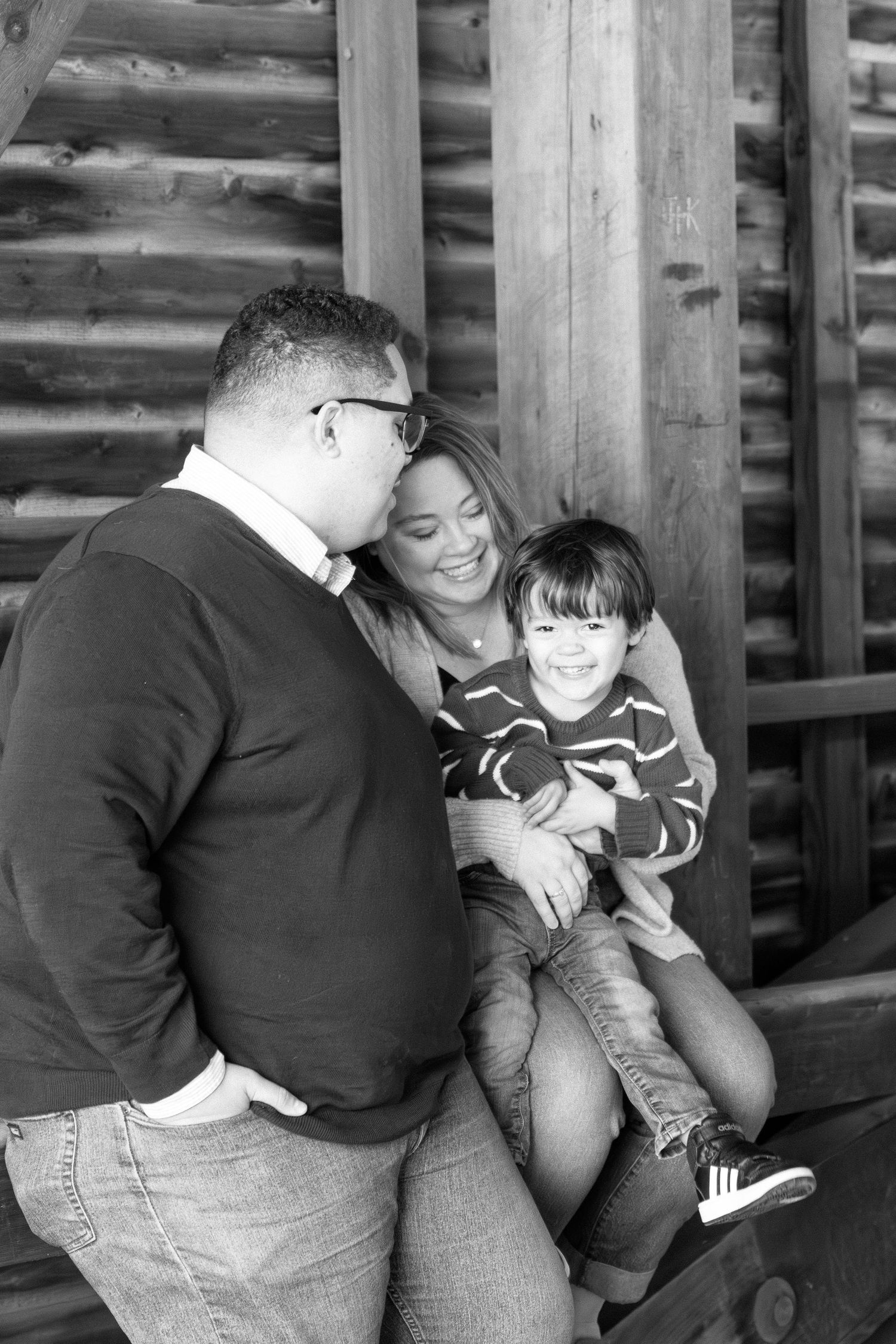 A tender black and white family moment captured on wooden steps outdoors in casual attire.