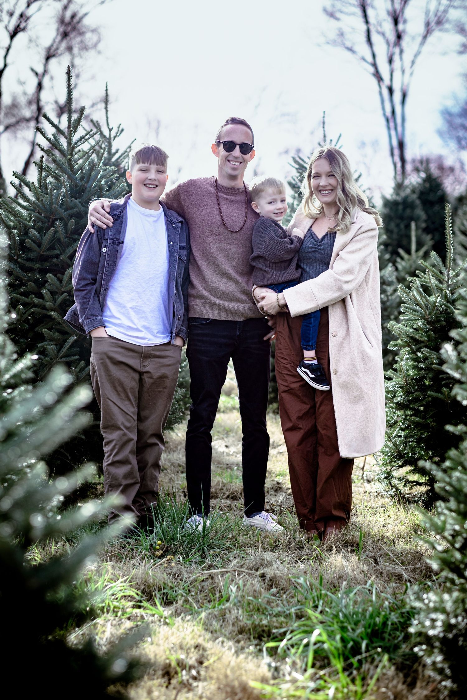 A group stands among evergreen Christmas trees during a winter tree shopping trip at a tree farm.