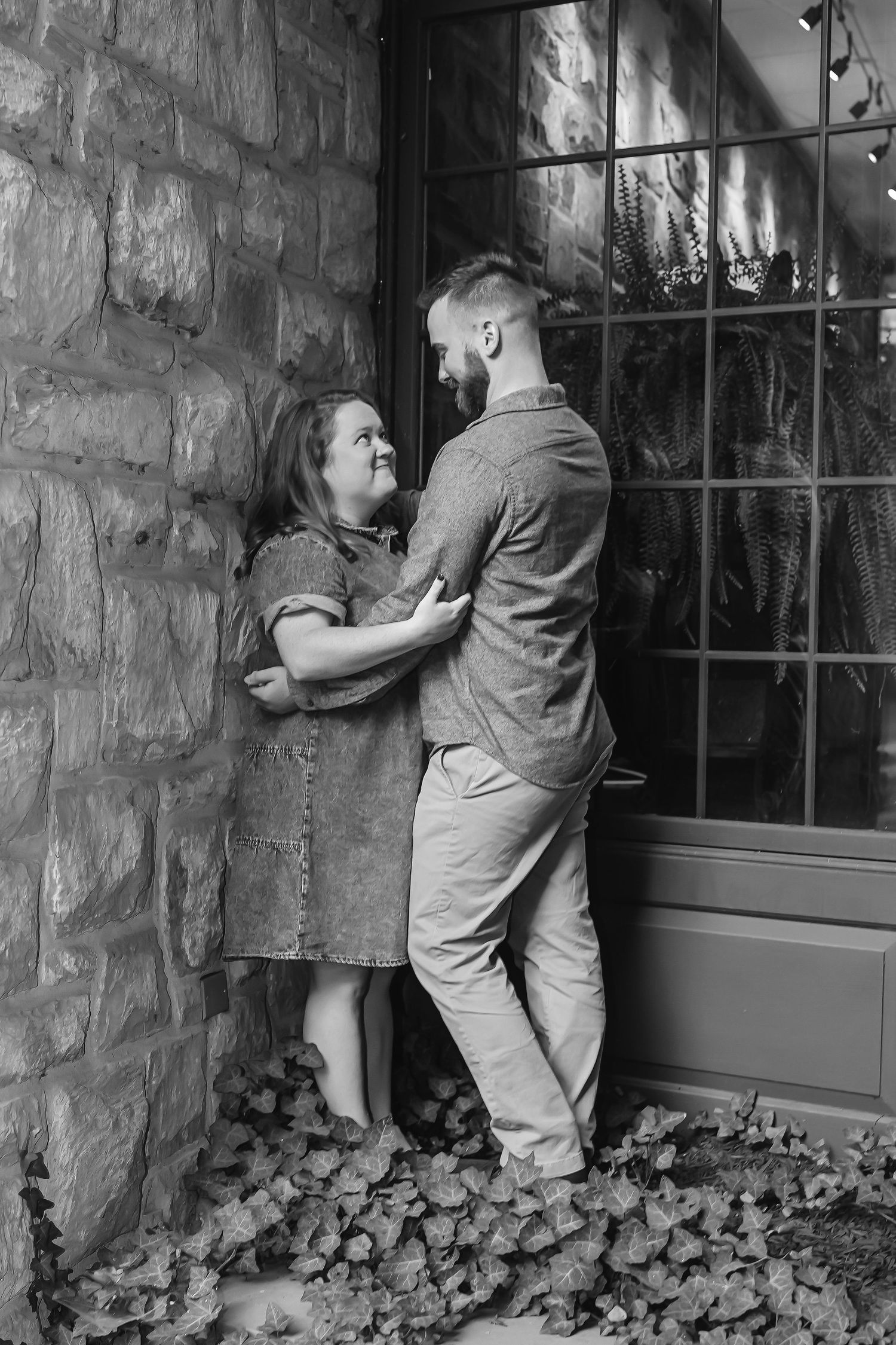 A sequence of playful black and white photos showing two people peeking through a stone wall window.