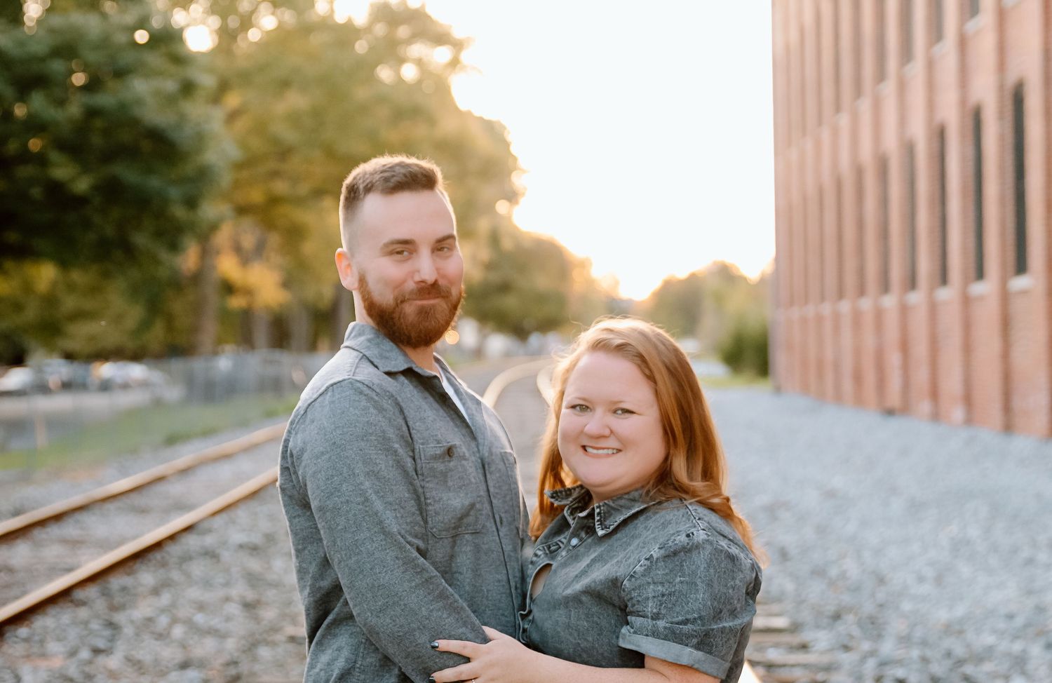 A couple in casual attire shares tender moments along train tracks during a golden hour photo session.