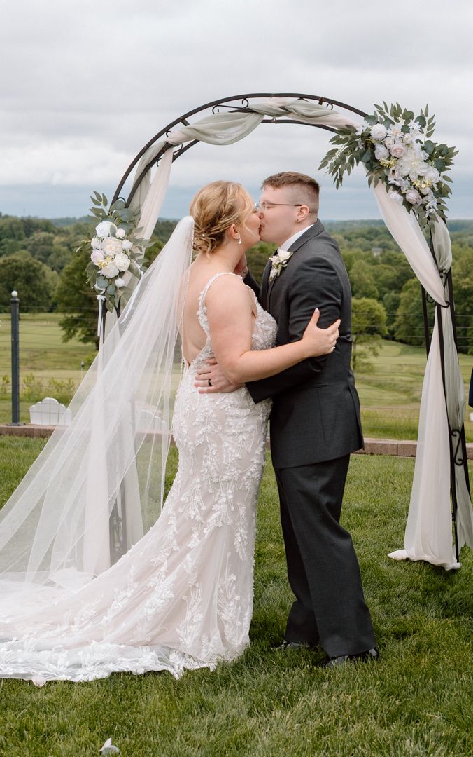 A wedding ceremony captured in sequence as a couple shares their first kiss under a floral-decorated arch in an outdoor field.