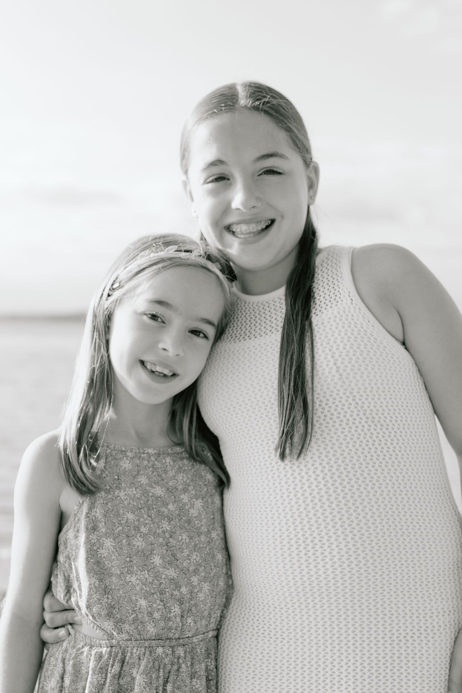 Mother and daughter in white summer outfits smiling at the beach.