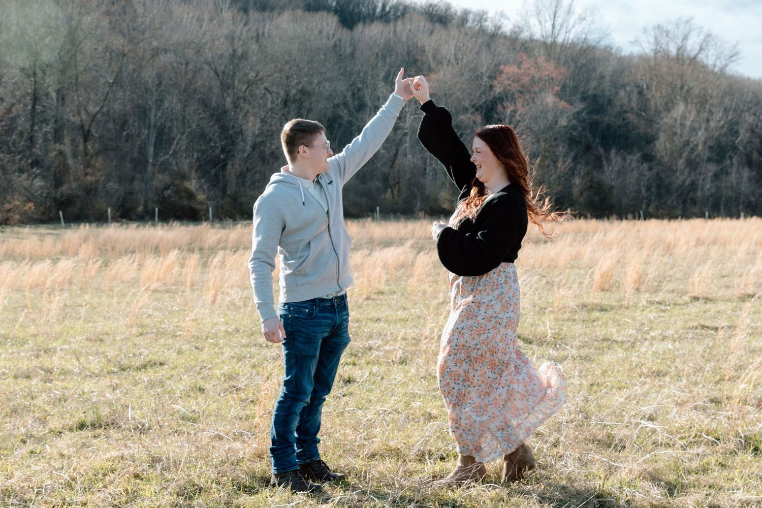 A couple dances in a golden field during autumn while holding hands and twirling.