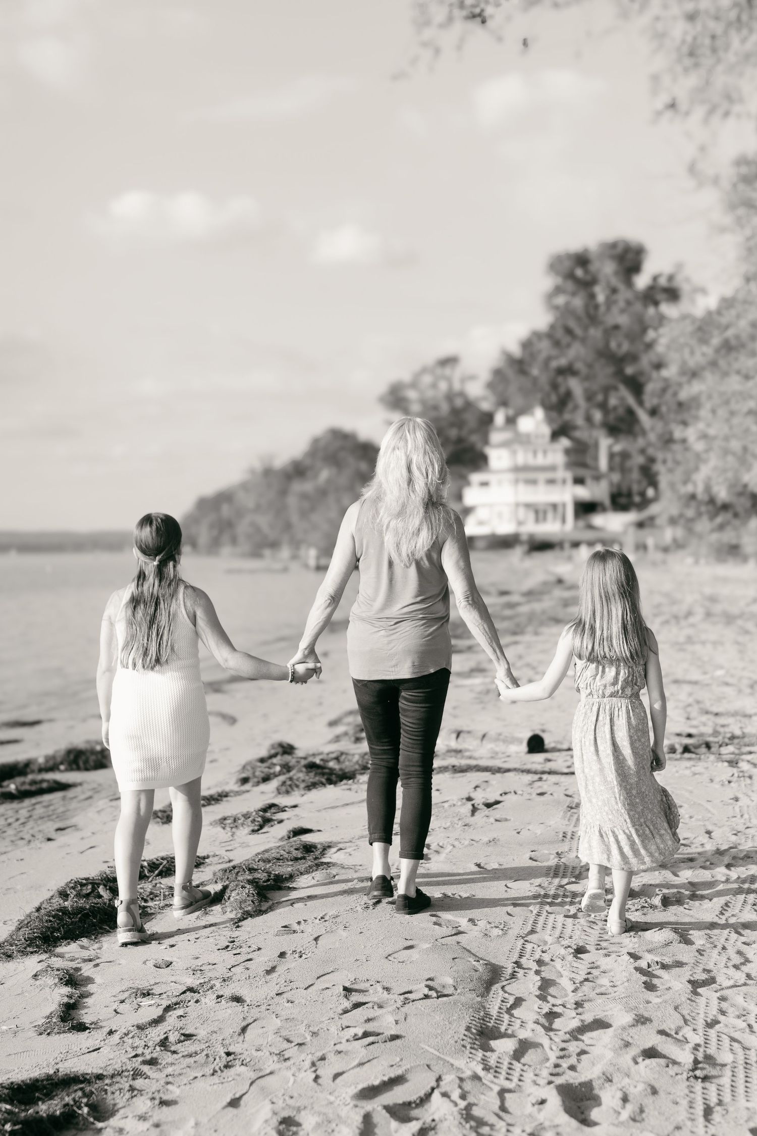 Family walking hand in hand along a sandy beach in black and white.