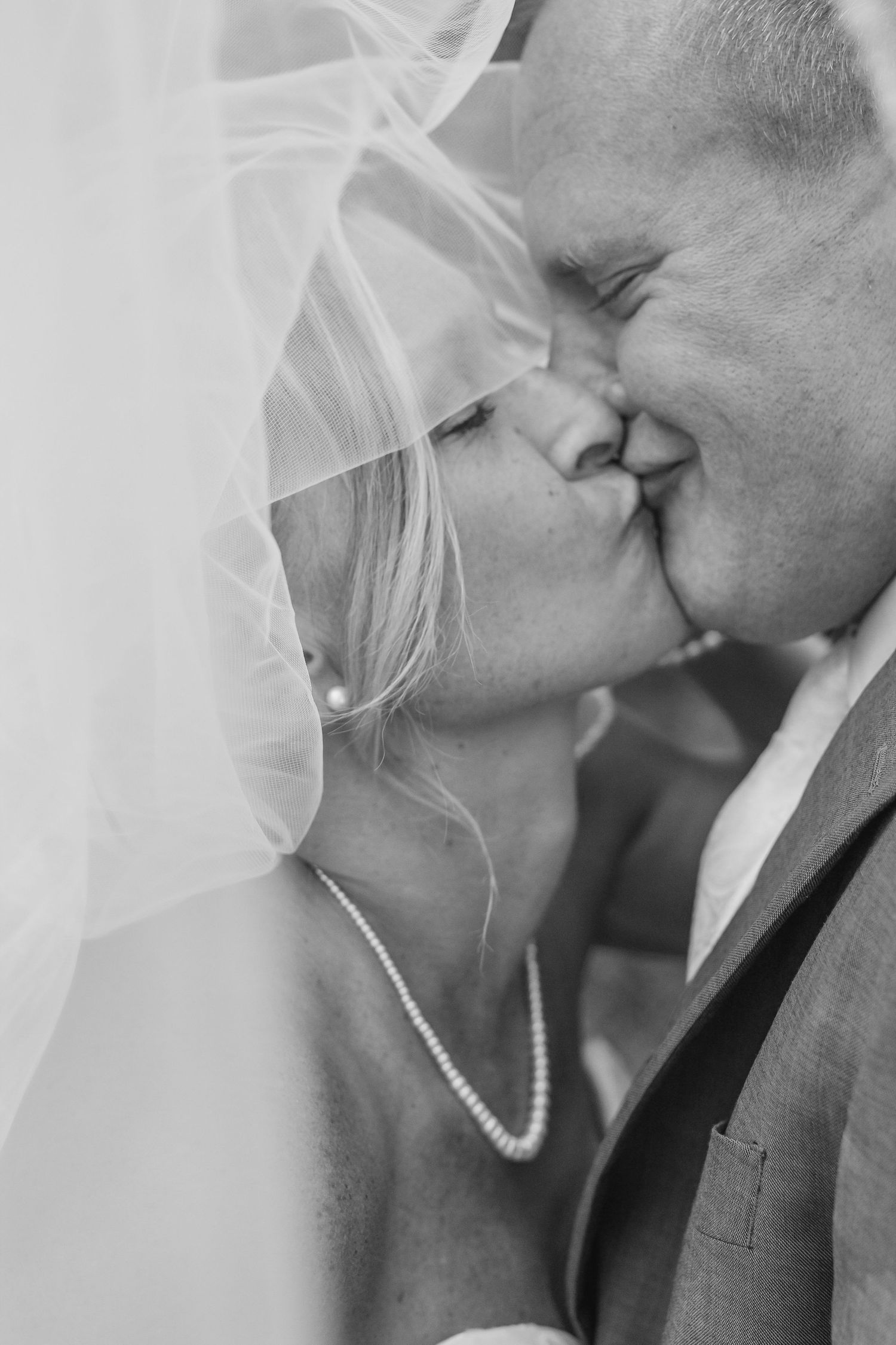 Romantic black and white portrait of a bride and groom sharing an intimate moment under a veil.